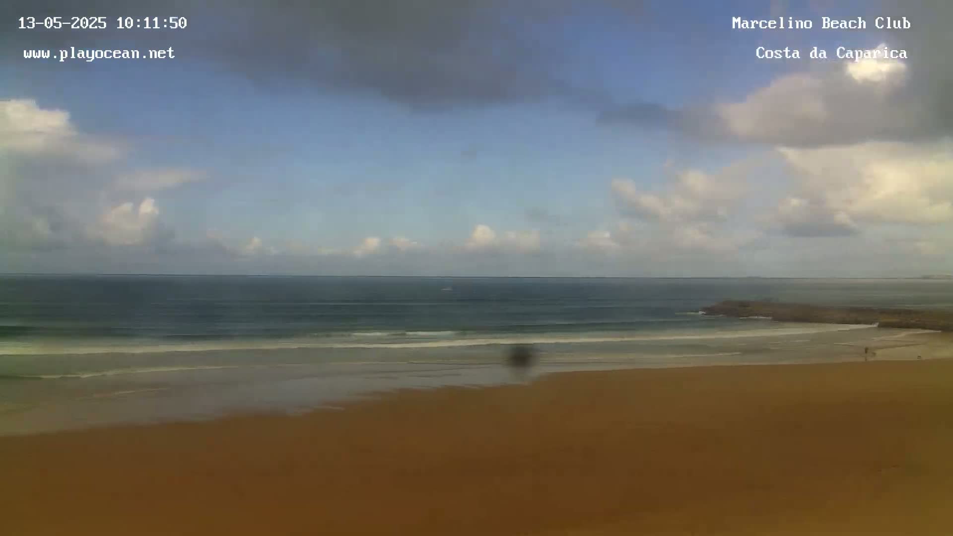 A sandy beach stretches out to a calm ocean under a partly cloudy sky.