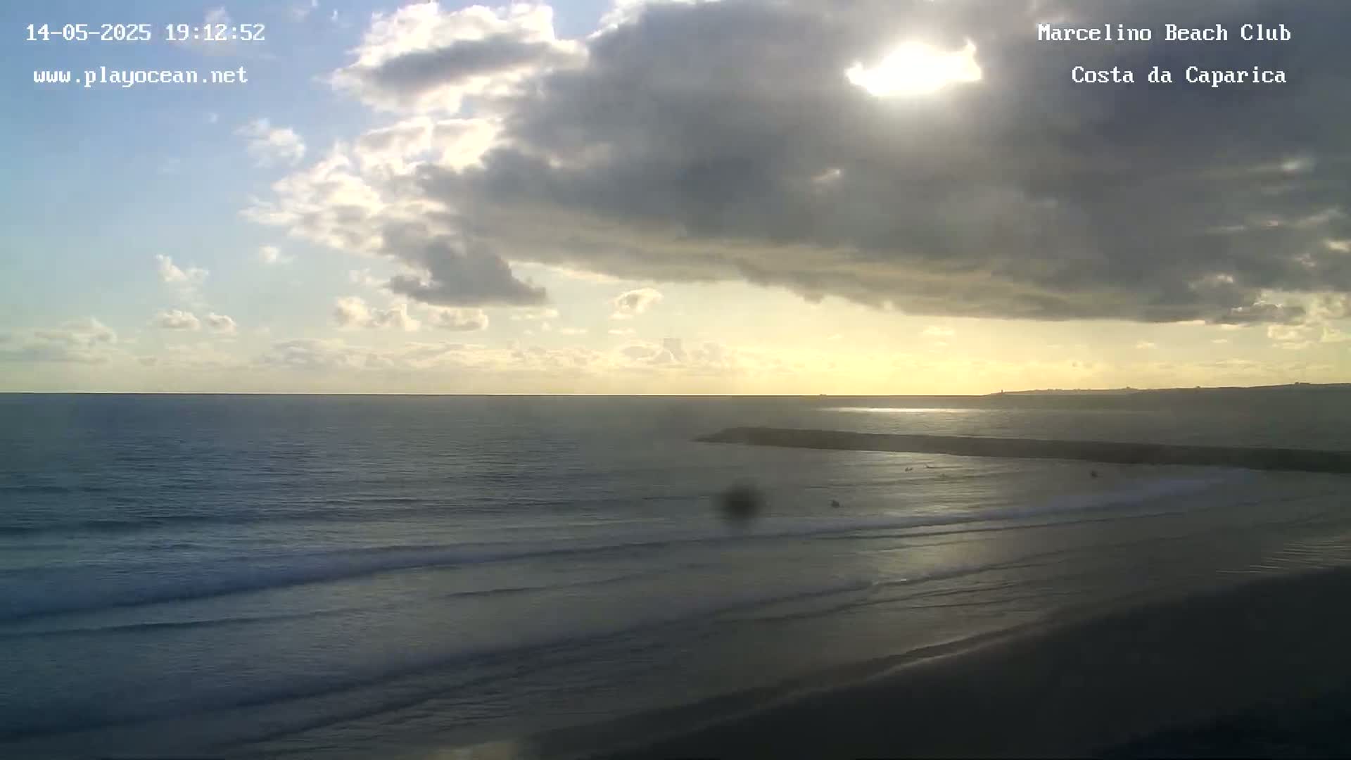 A partly cloudy sunset over a calm ocean beach with gentle waves rolling onto the shore.
