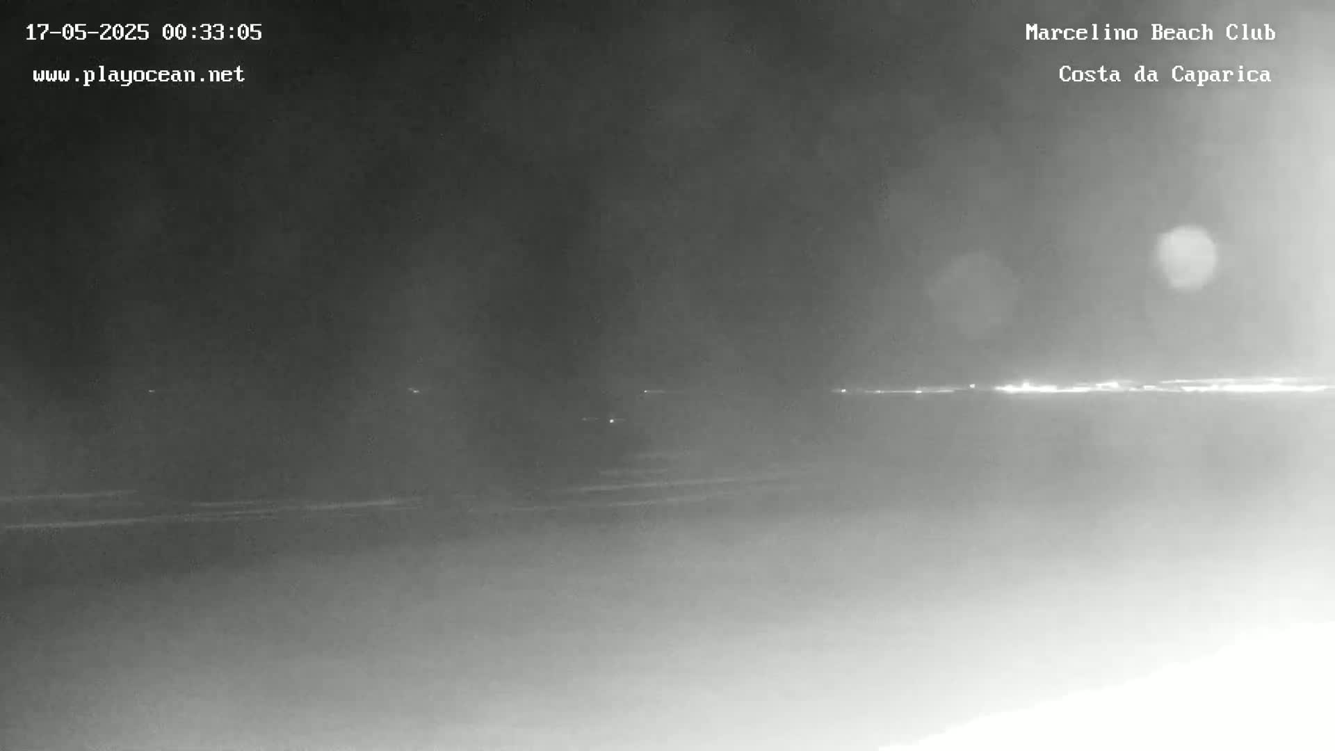 A nighttime, low-light image shows a dark beach and a distant, faintly lit horizon.