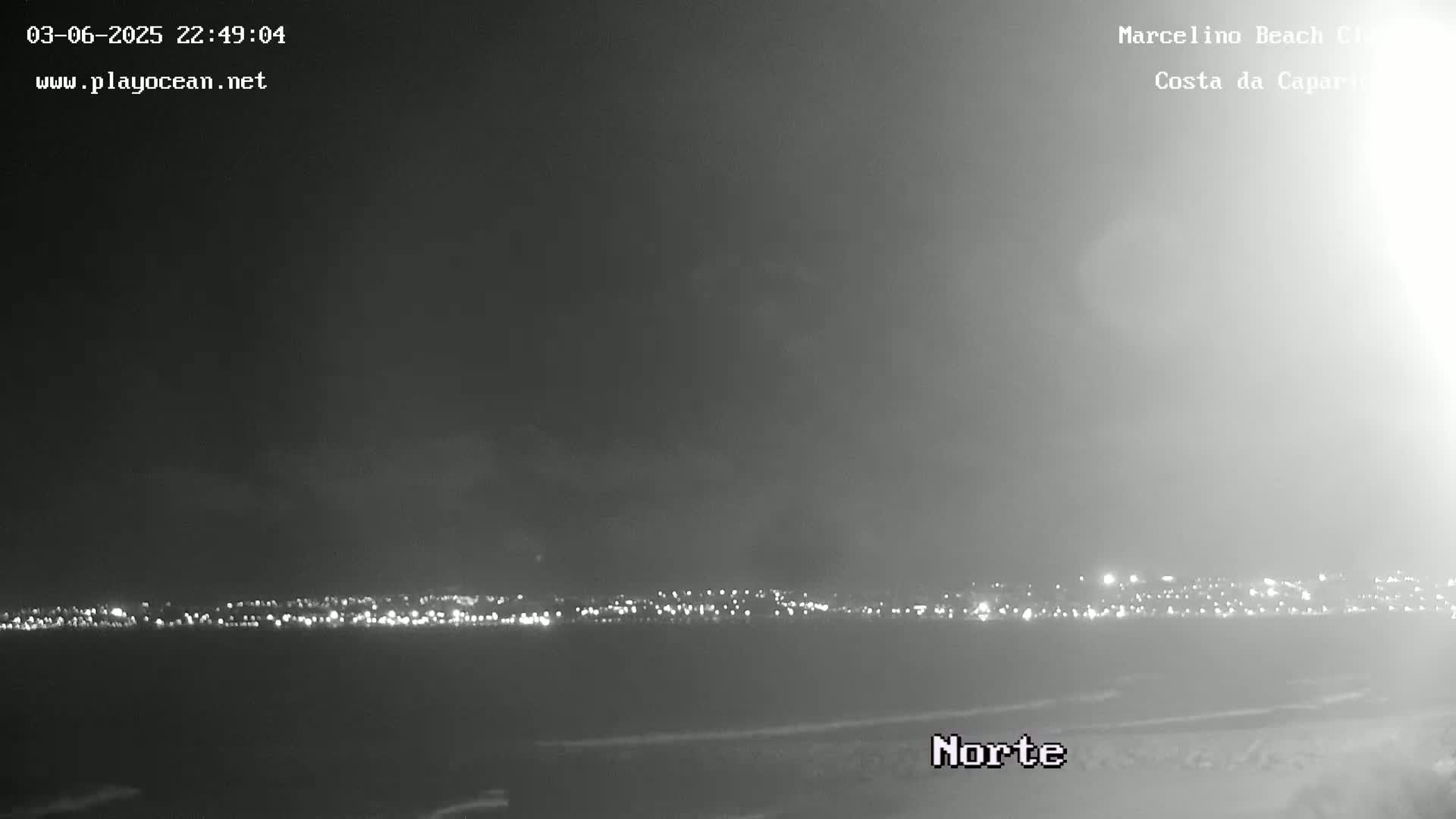 A nighttime, hazy view shows a distant city skyline illuminated by lights across a dark body of water.