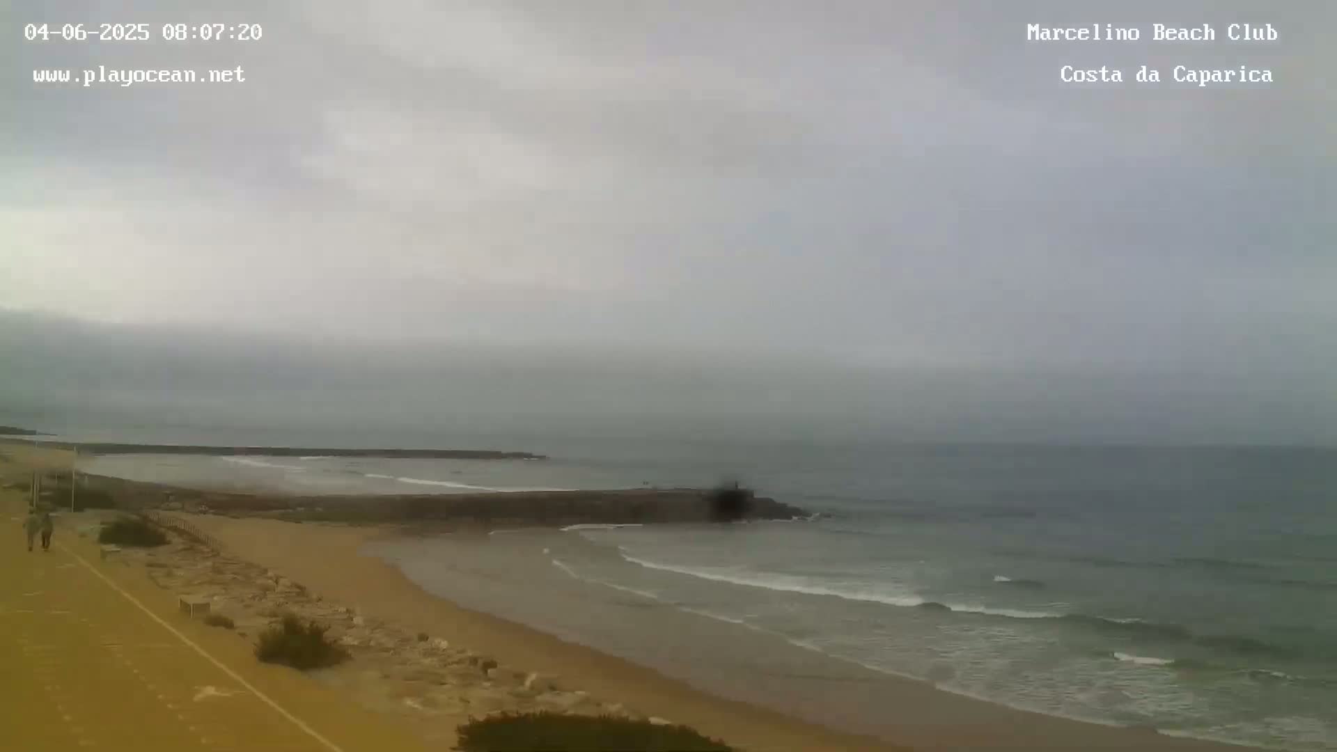 A sandy beach with a calm ocean under an overcast sky.