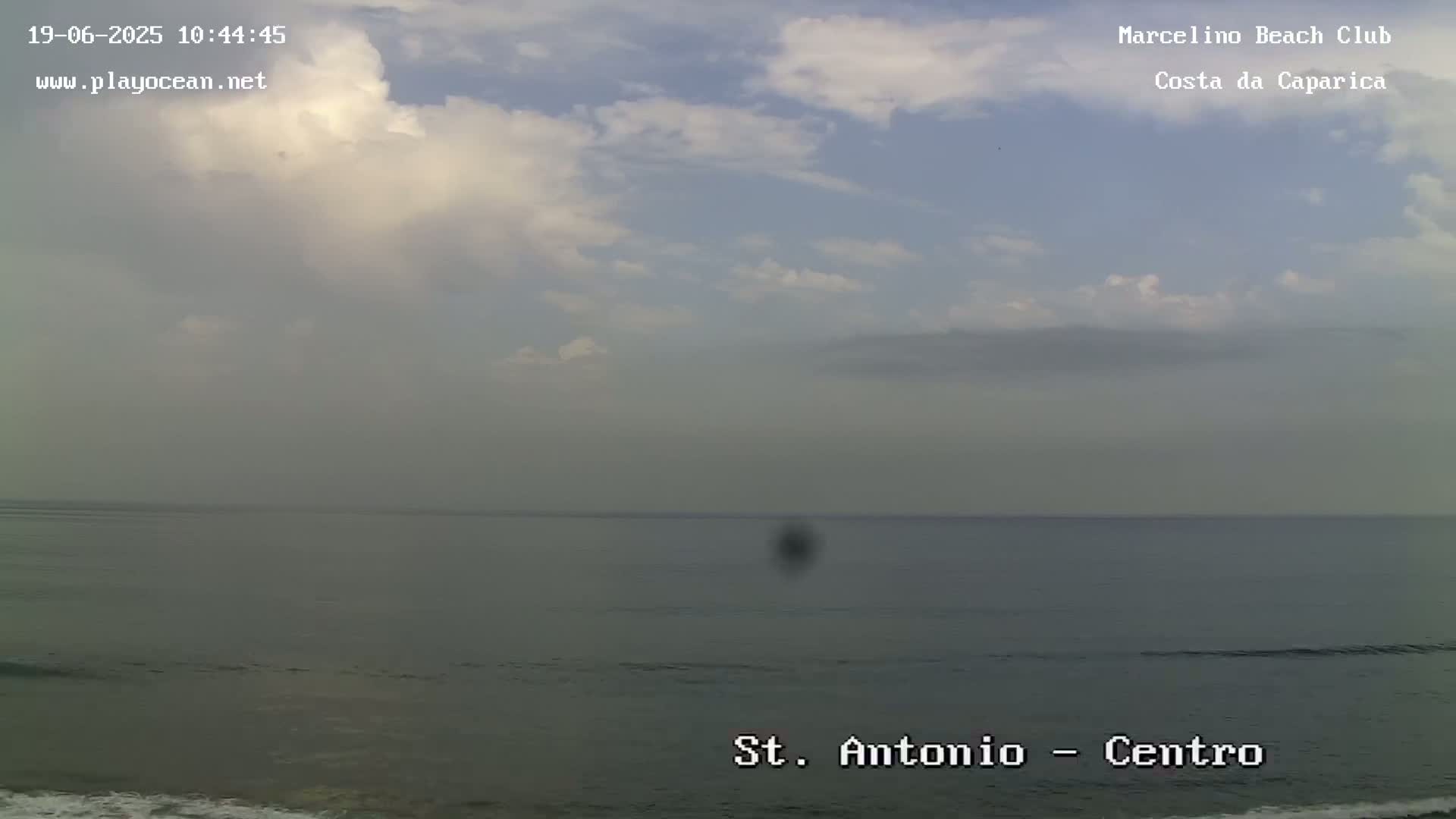A mostly cloudy sky overlooks a calm ocean.