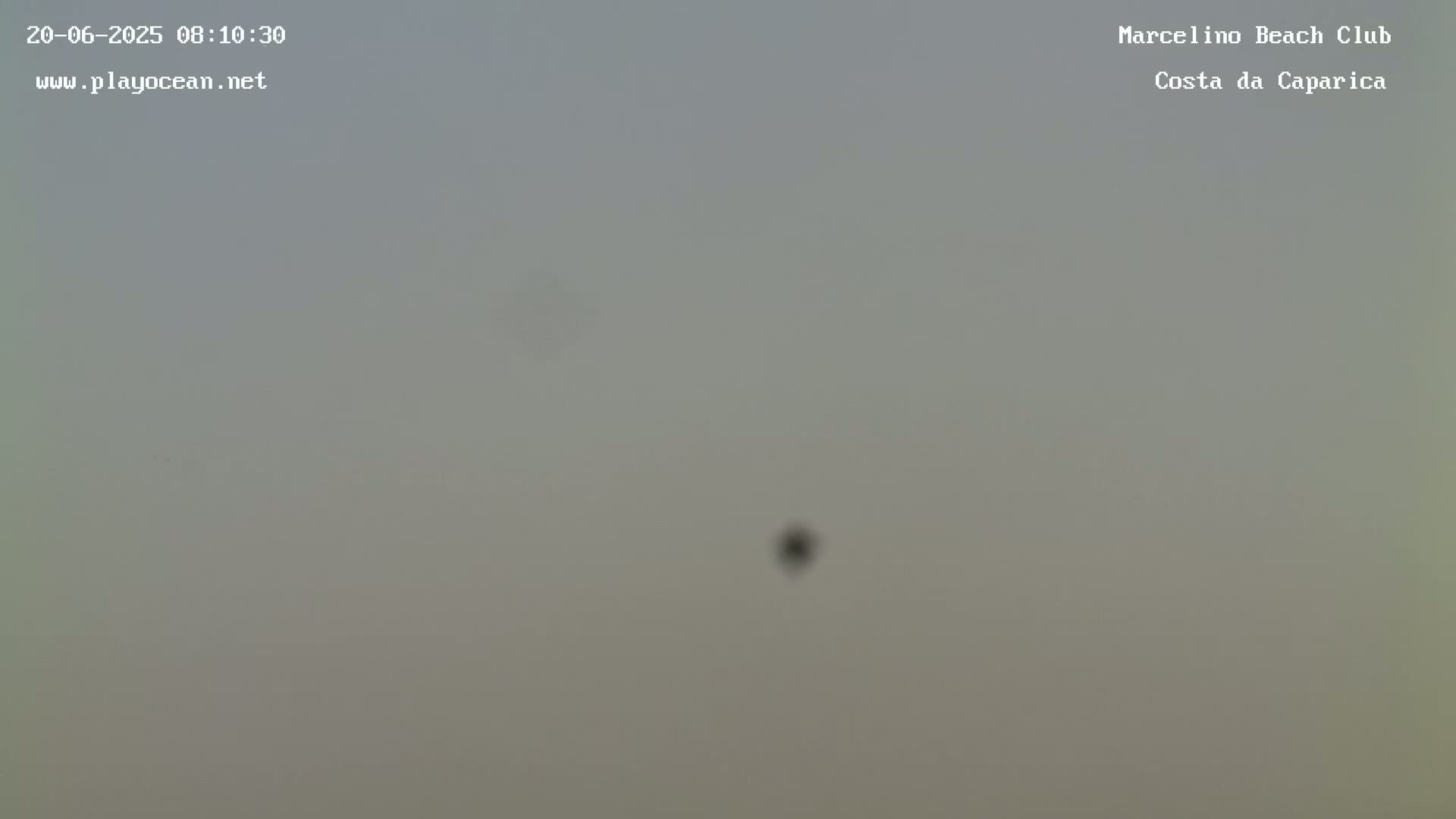 A hazy, overcast sky is visible, with a small, dark object faintly seen in the center.