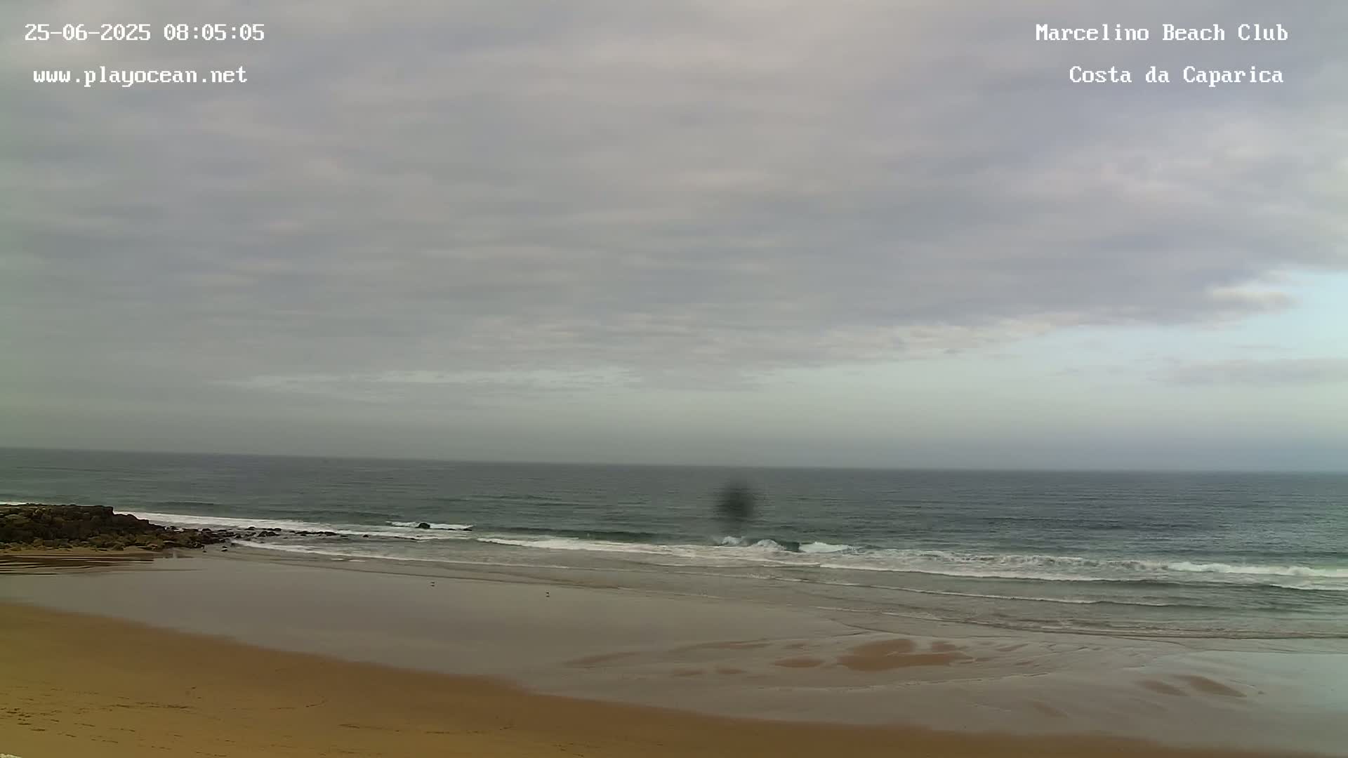 A mostly cloudy sky hangs over a sandy beach with gentle waves rolling onto the shore.