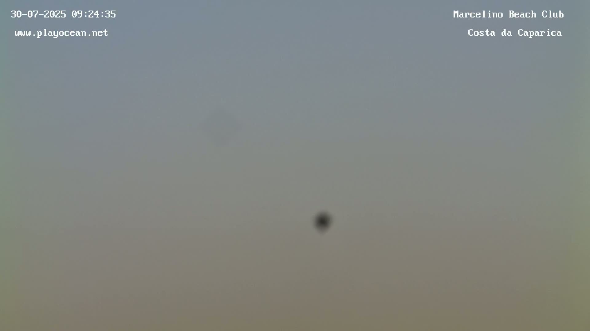 A hazy, overcast sky is visible with a small, dark object in the center.