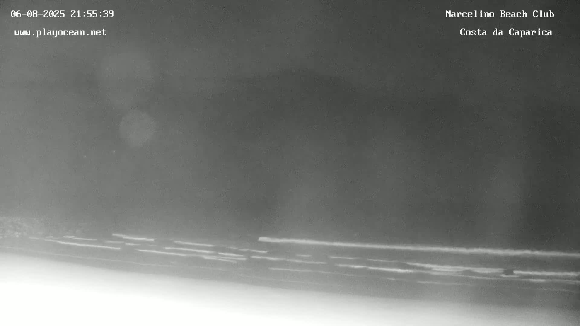 A nighttime, low-light image shows dark ocean waves gently lapping the shore.