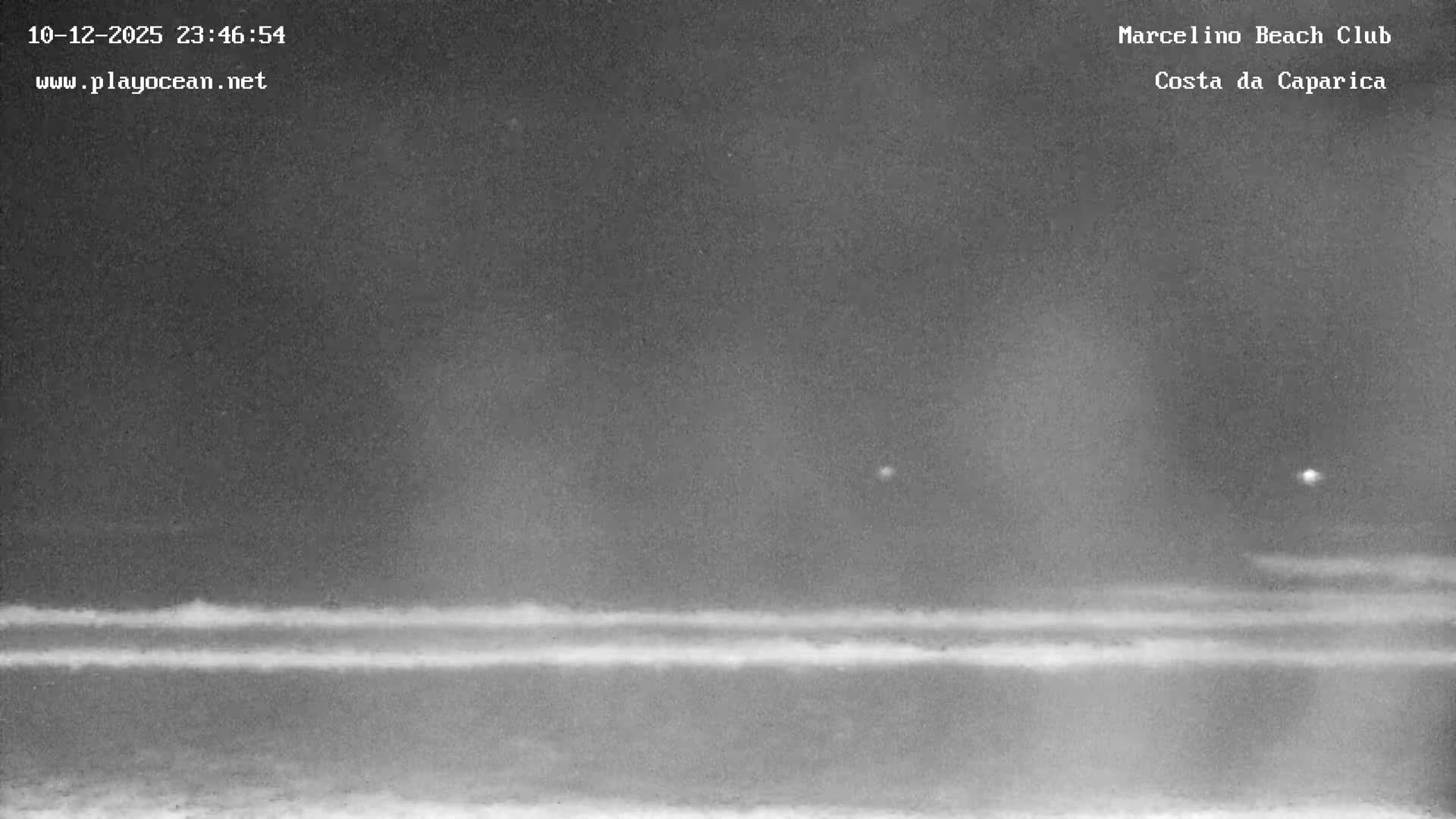 A grayscale outdoor scene at night depicts a clear sky above a vast body of water, marked by two distinct bright lights and several horizontal bands of light or wave patterns stretching across its surface.