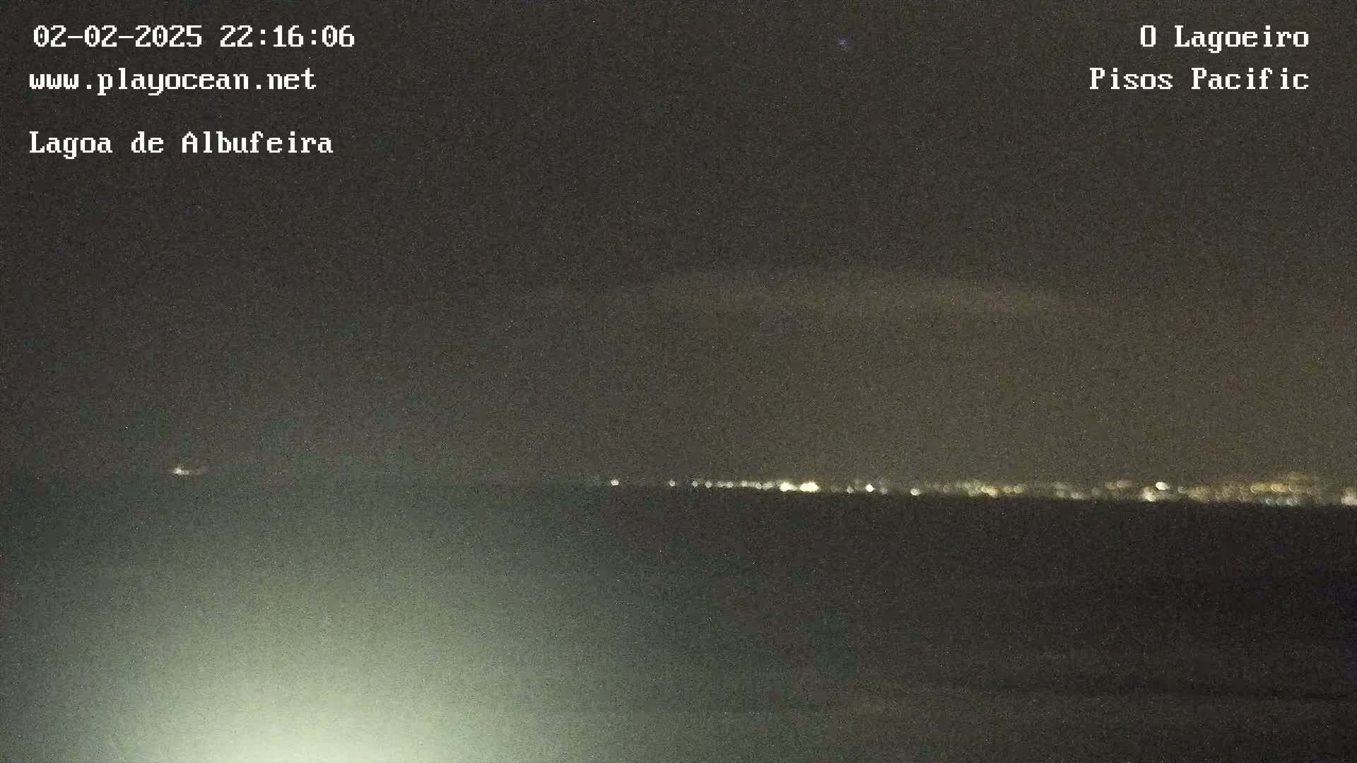 A nighttime long shot shows a dark body of water with a faint line of distant lights on the horizon under a mostly clear, dark sky.