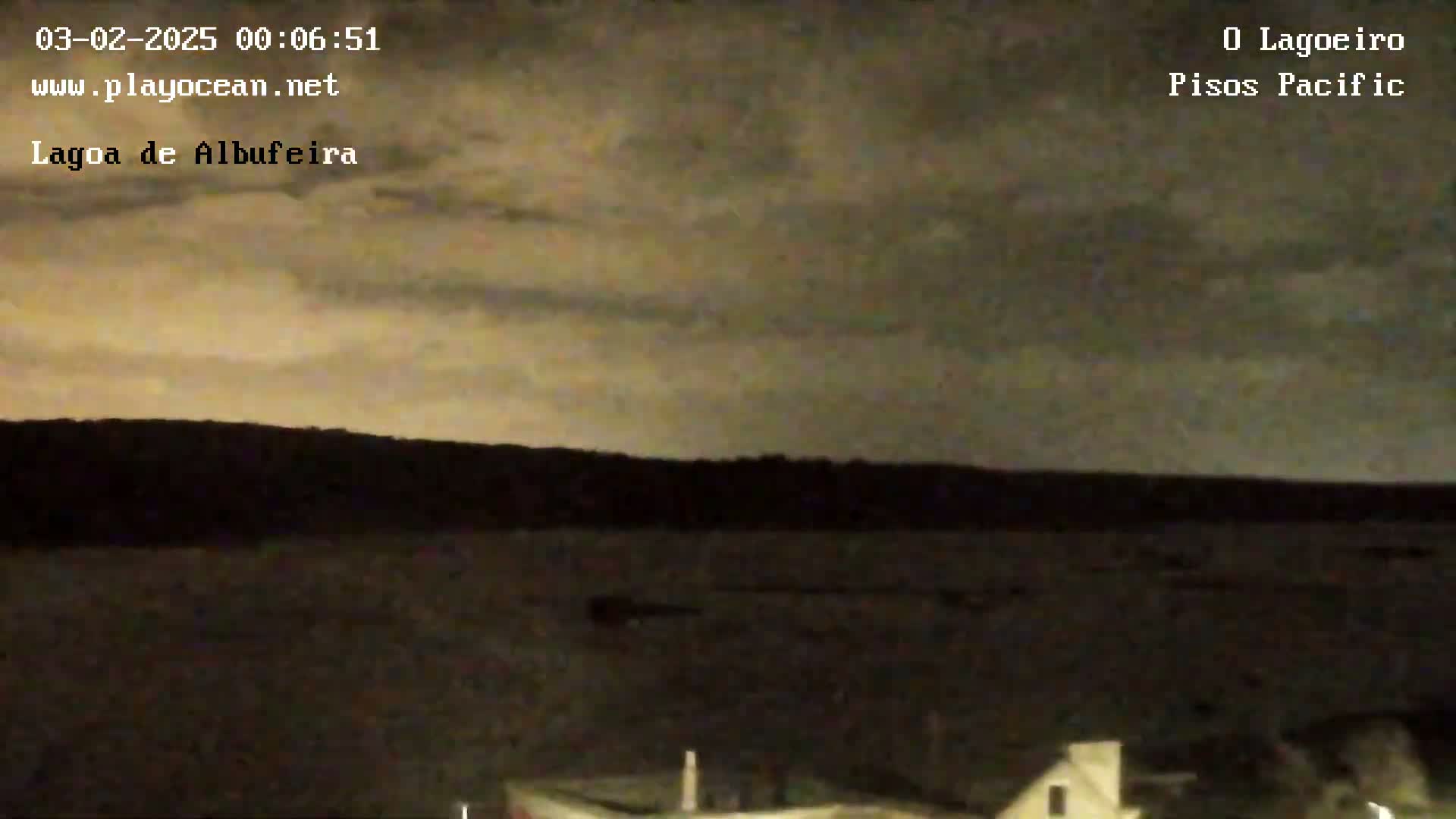 A nighttime view of a body of water under a mostly cloudy sky shows a dark shoreline in the distance.