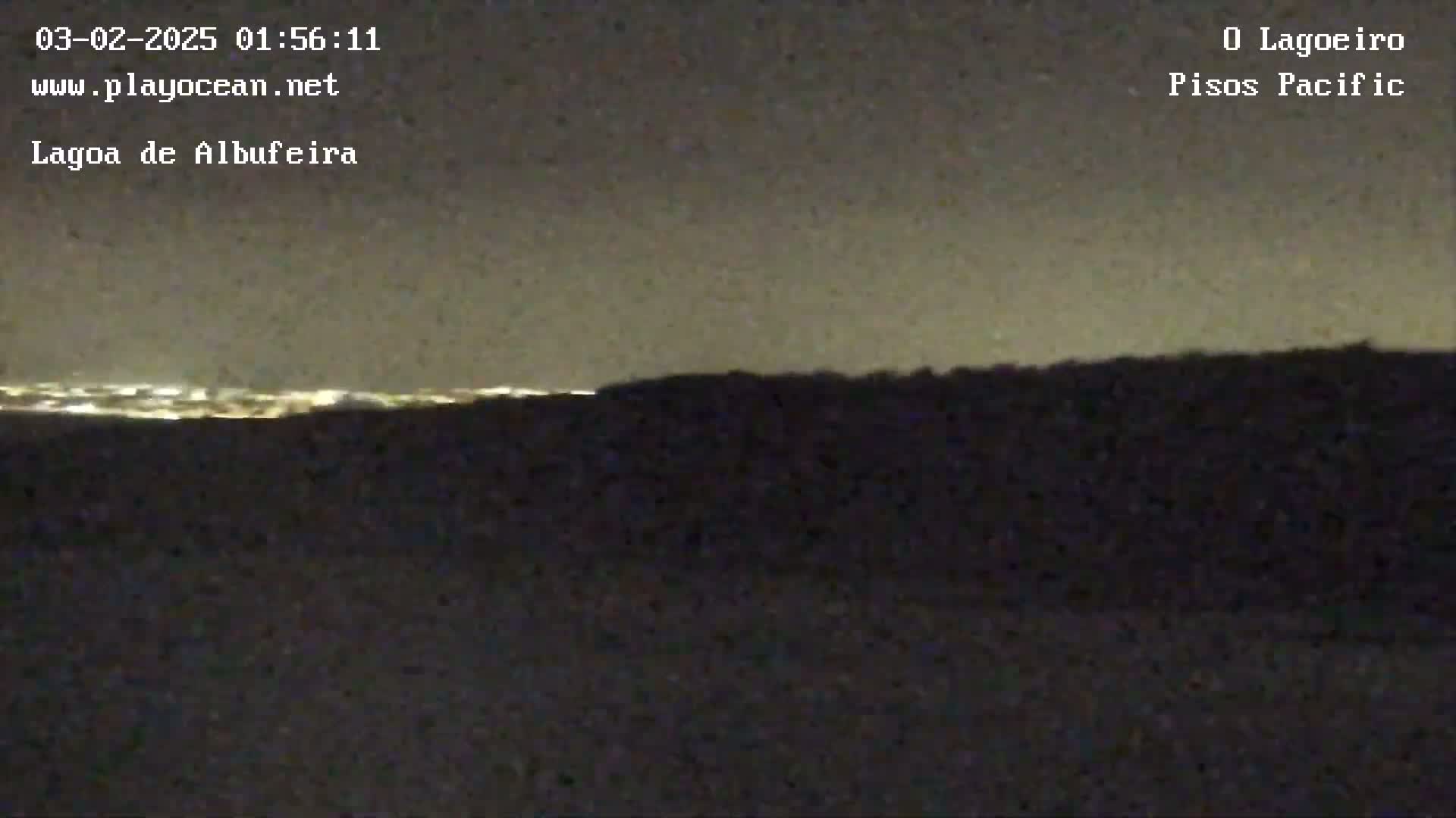 A nighttime view shows a dark landscape with a distant horizon line illuminated by city lights under a clear, dark sky.
