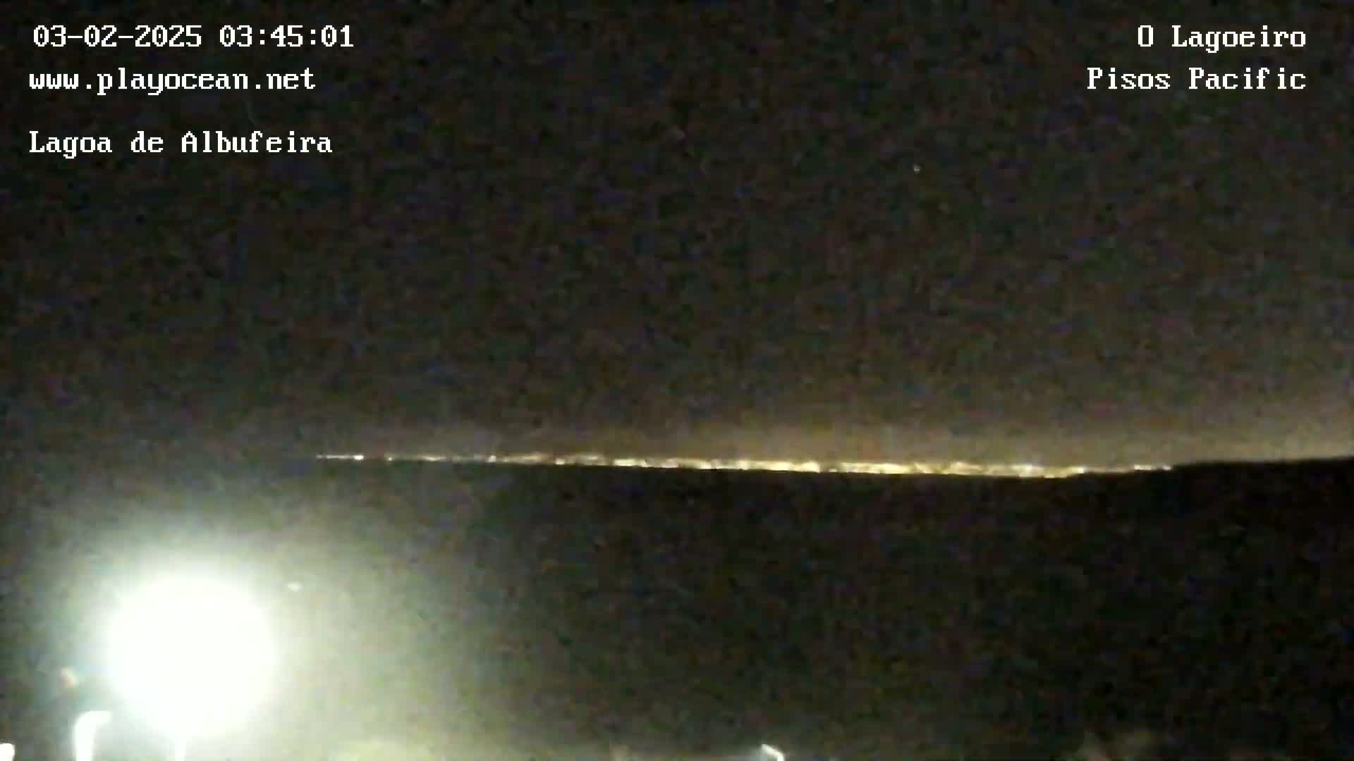A nighttime long shot shows a distant line of city lights on the horizon under a clear, dark sky.