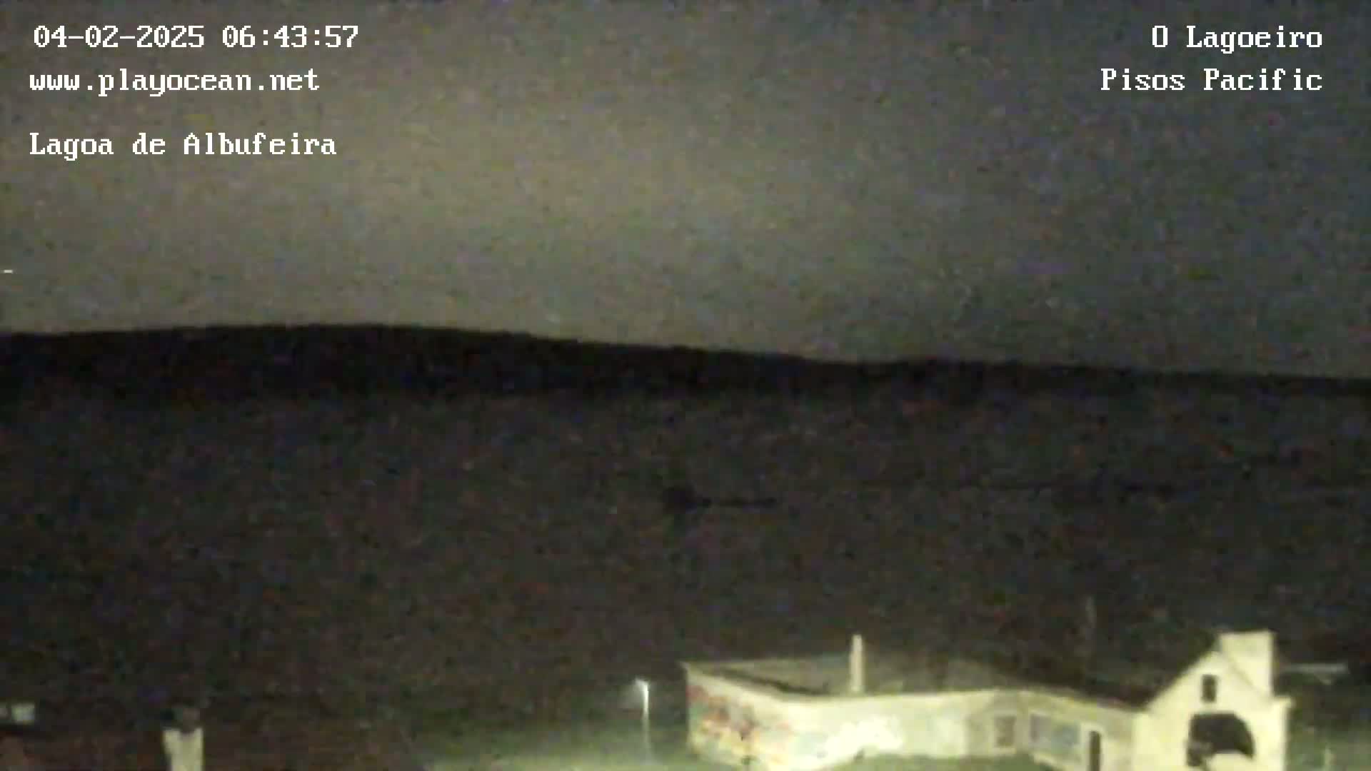 A dark, nighttime scene shows a flat, dark landscape with a building visible in the bottom right corner under a mostly clear, dark sky.
