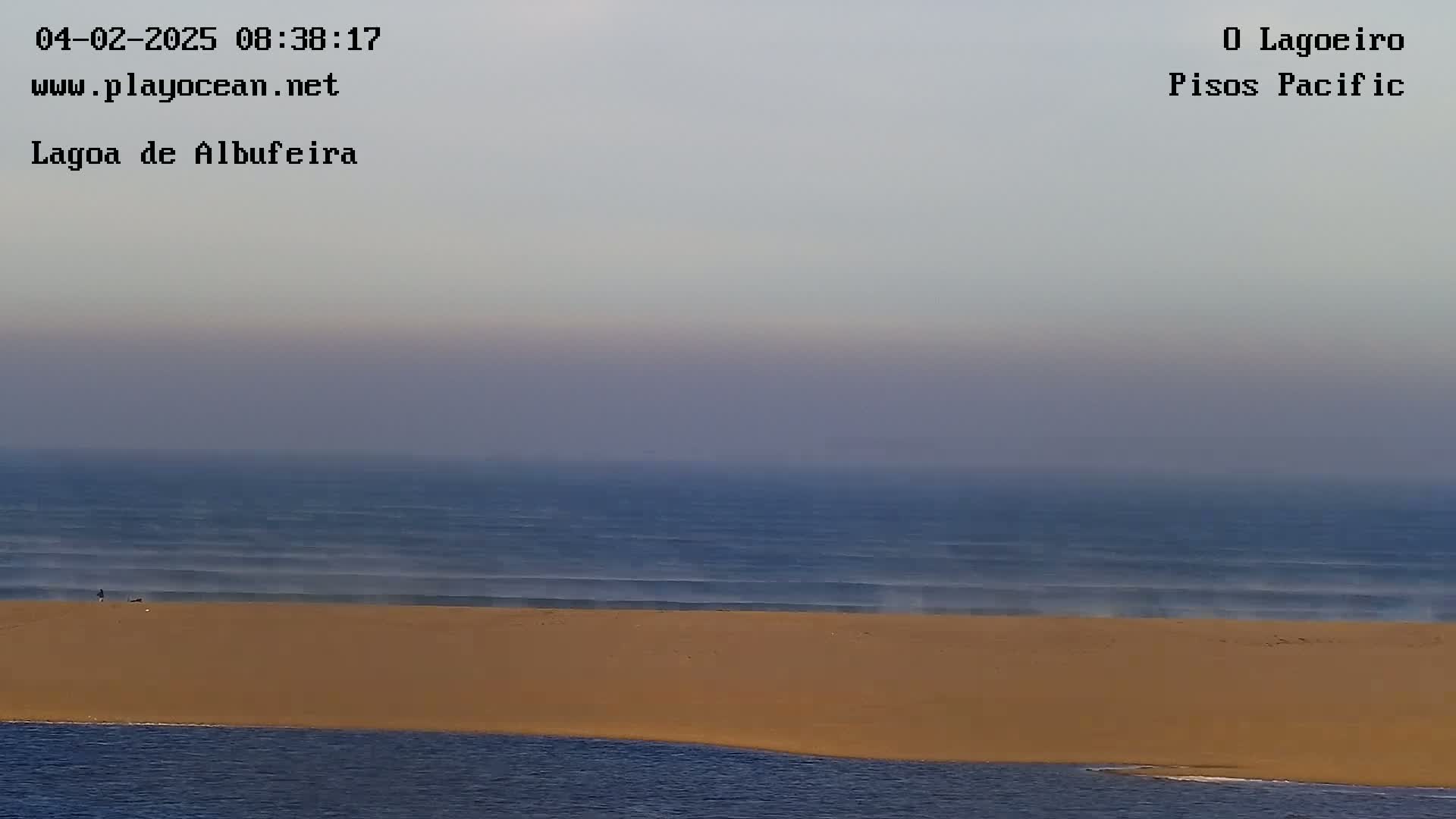 A hazy, light-blue ocean meets a wide, tan sandbar under a muted sky.