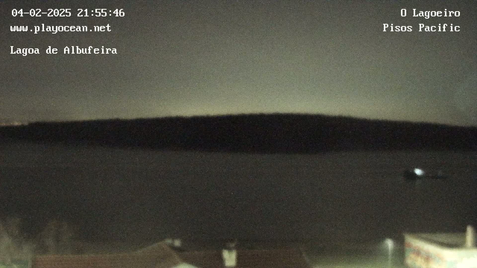 A dark body of water is seen at night under a dusky sky, with a dark landmass in the distance.