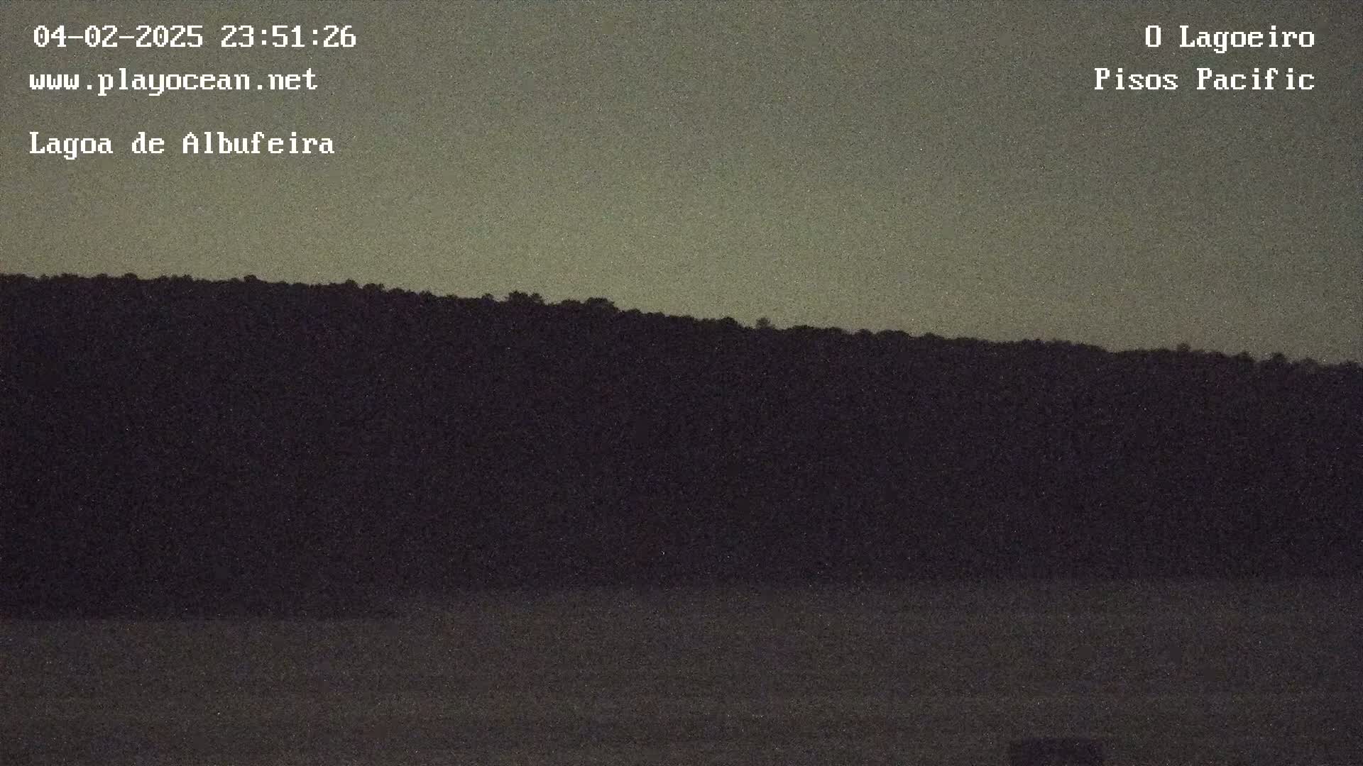 A dark, silhouetted hill rises above a calm body of water under a dusky sky.