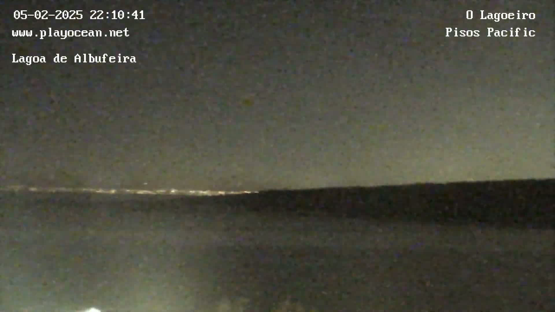 A nighttime long shot shows a dark body of water with a distant line of city lights under a mostly clear, dark sky.