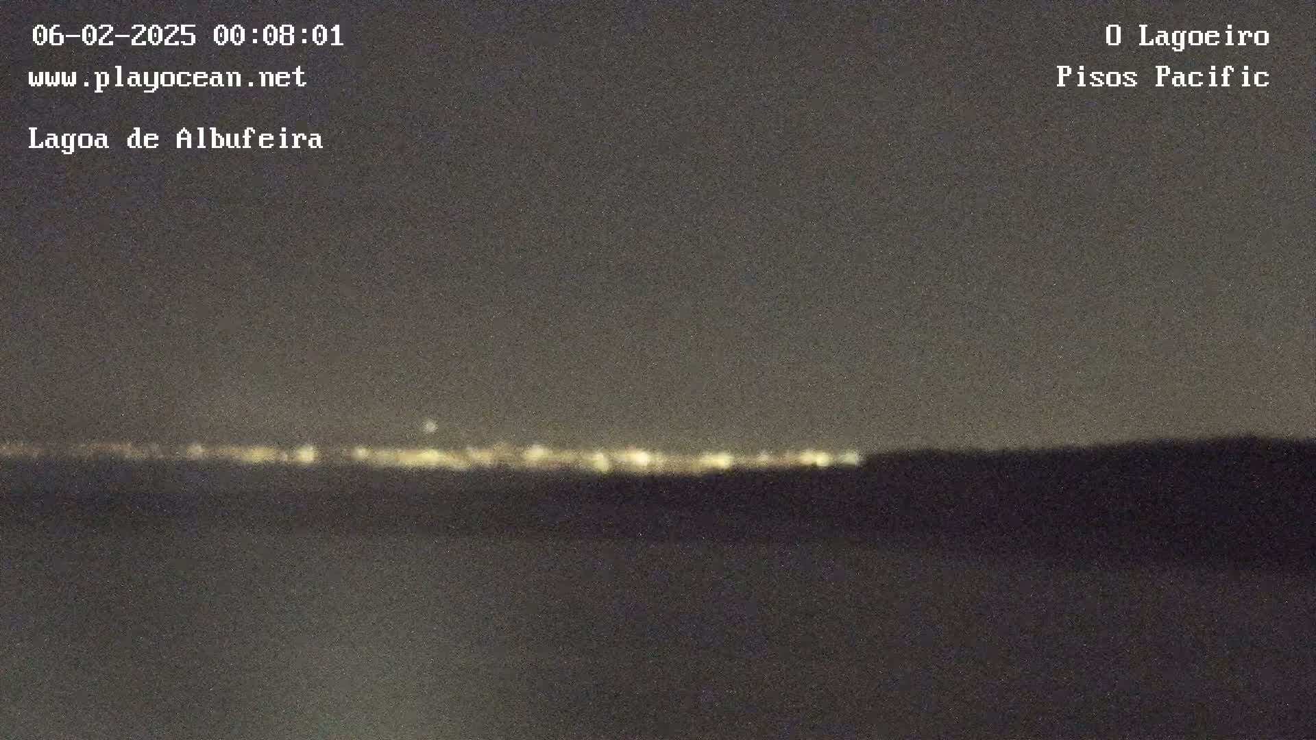 A nighttime view of a dark body of water with a distant line of city lights on the horizon under a clear, dark sky.