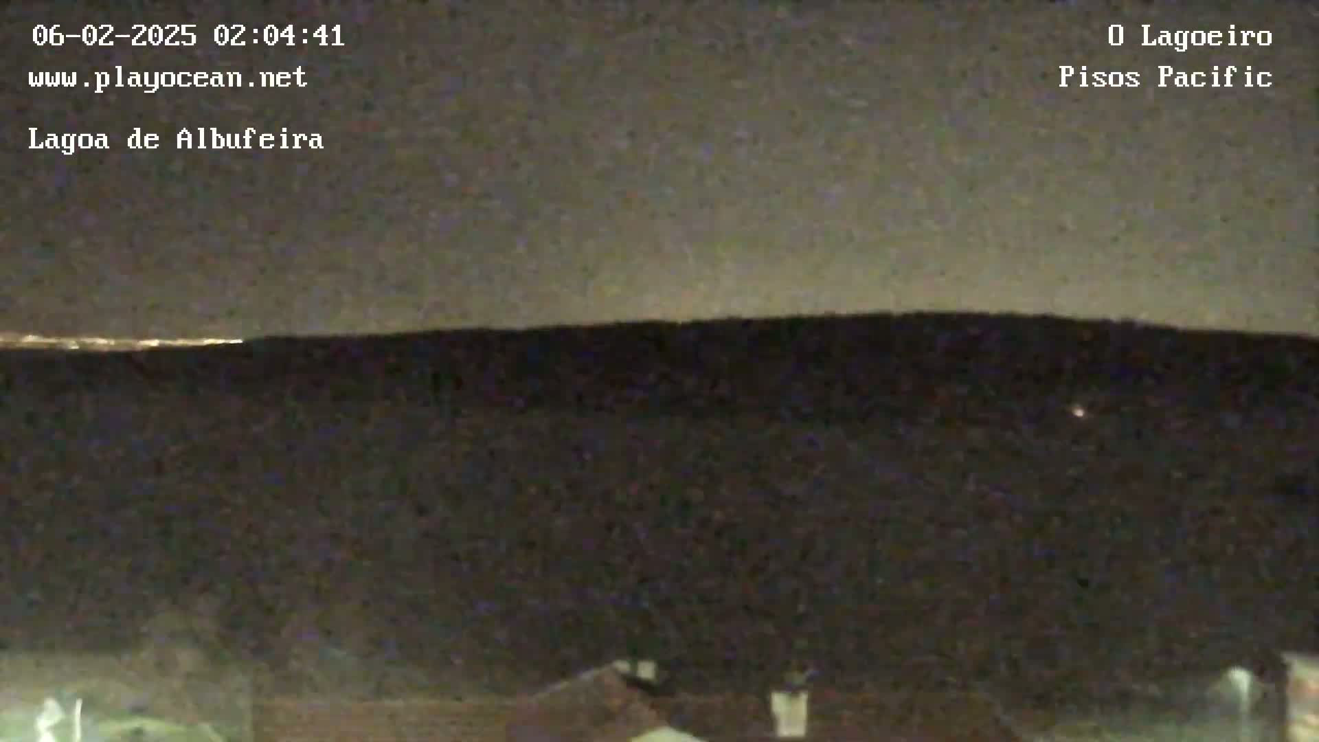 A dark, nighttime landscape is shown with a faint, low horizon light, possibly city lights, visible on the horizon.
