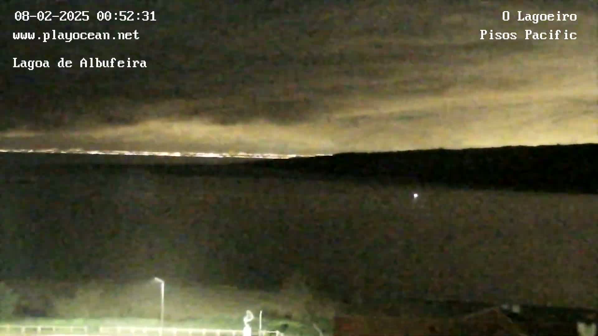 A nighttime view of a body of water under a cloudy sky, with a faint light on the horizon.