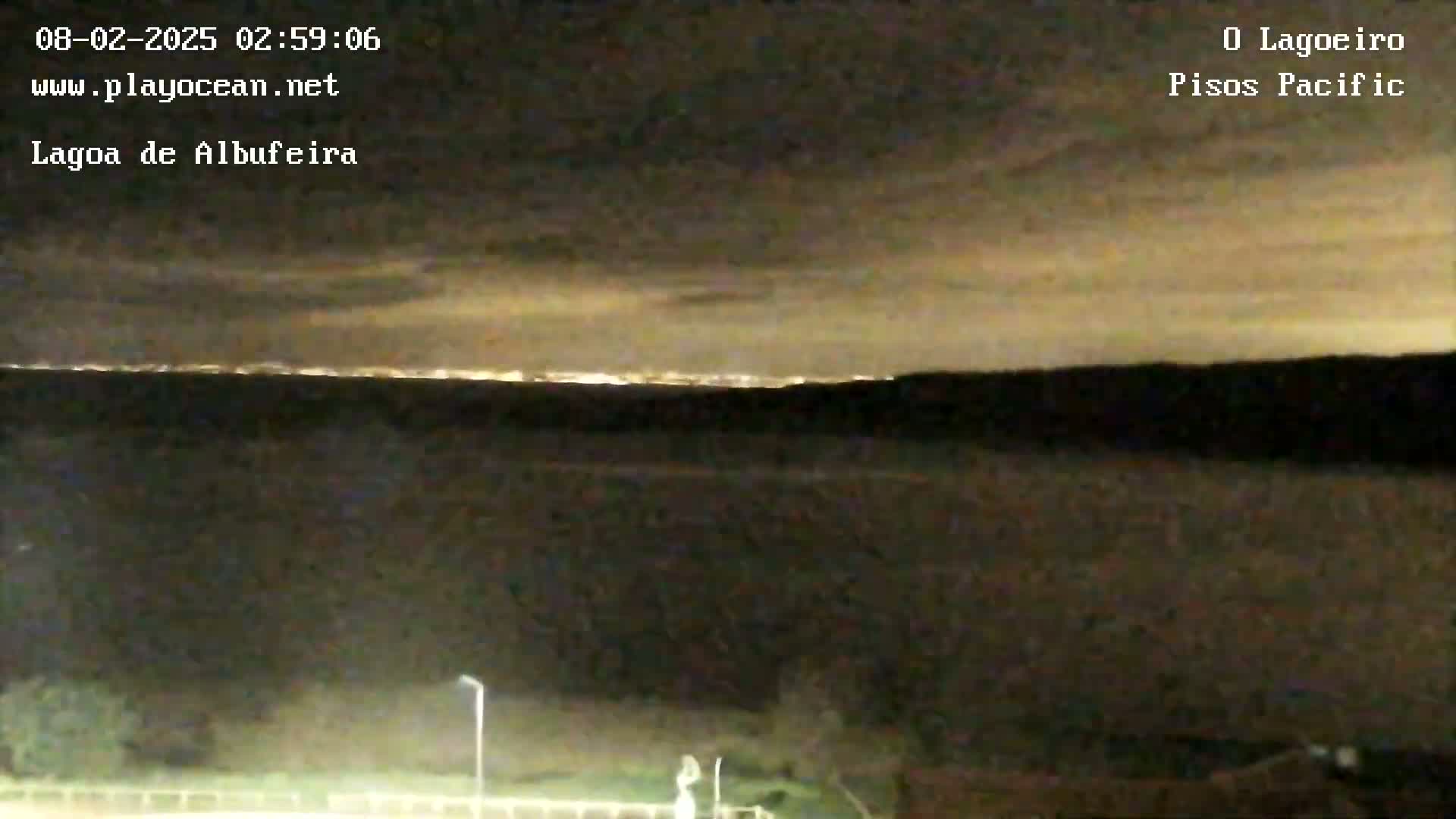 A nighttime view shows a body of water under a cloudy sky, with city lights faintly visible on the horizon.