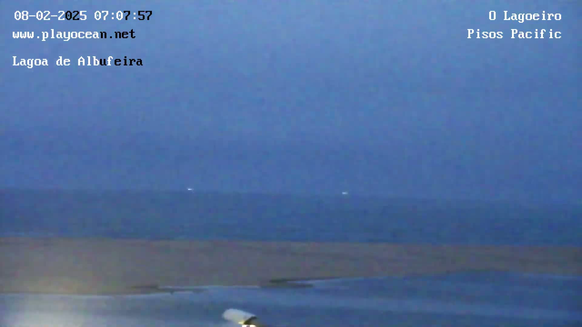 A mostly overcast, dark blue sky hangs over a calm body of water with a light-colored sandy shore in the foreground.