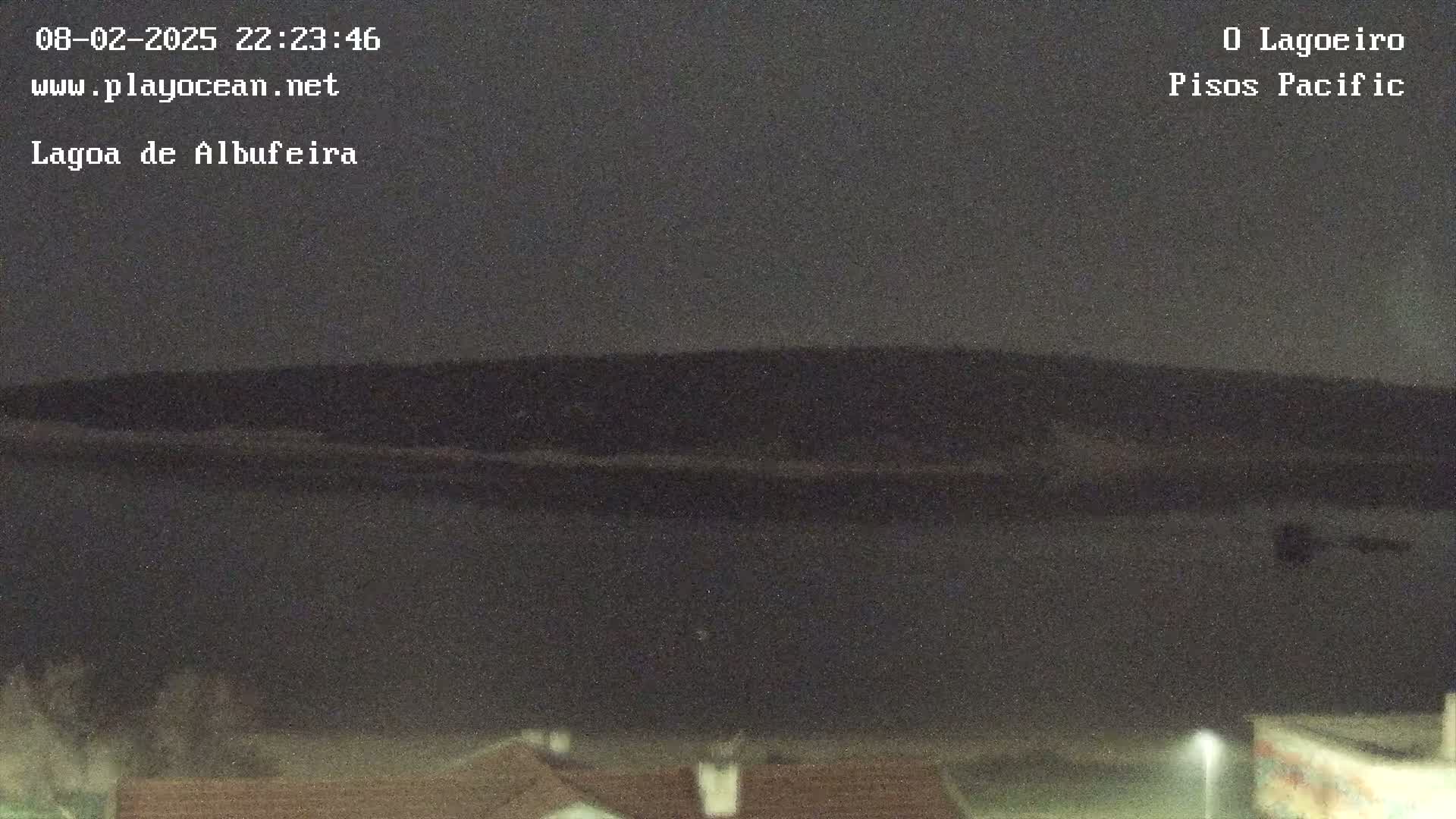A dark, nighttime view of a body of water with a dark shoreline and hills in the background.