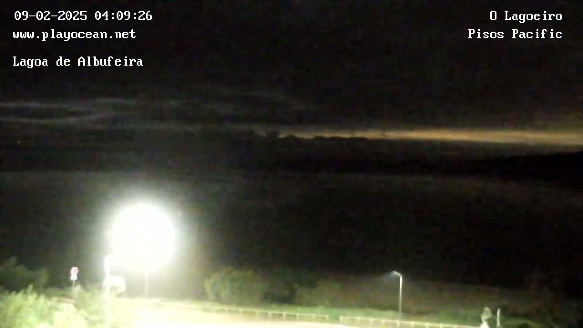 A nighttime view of a dark body of water under a cloudy sky illuminated by a bright light source in the foreground.