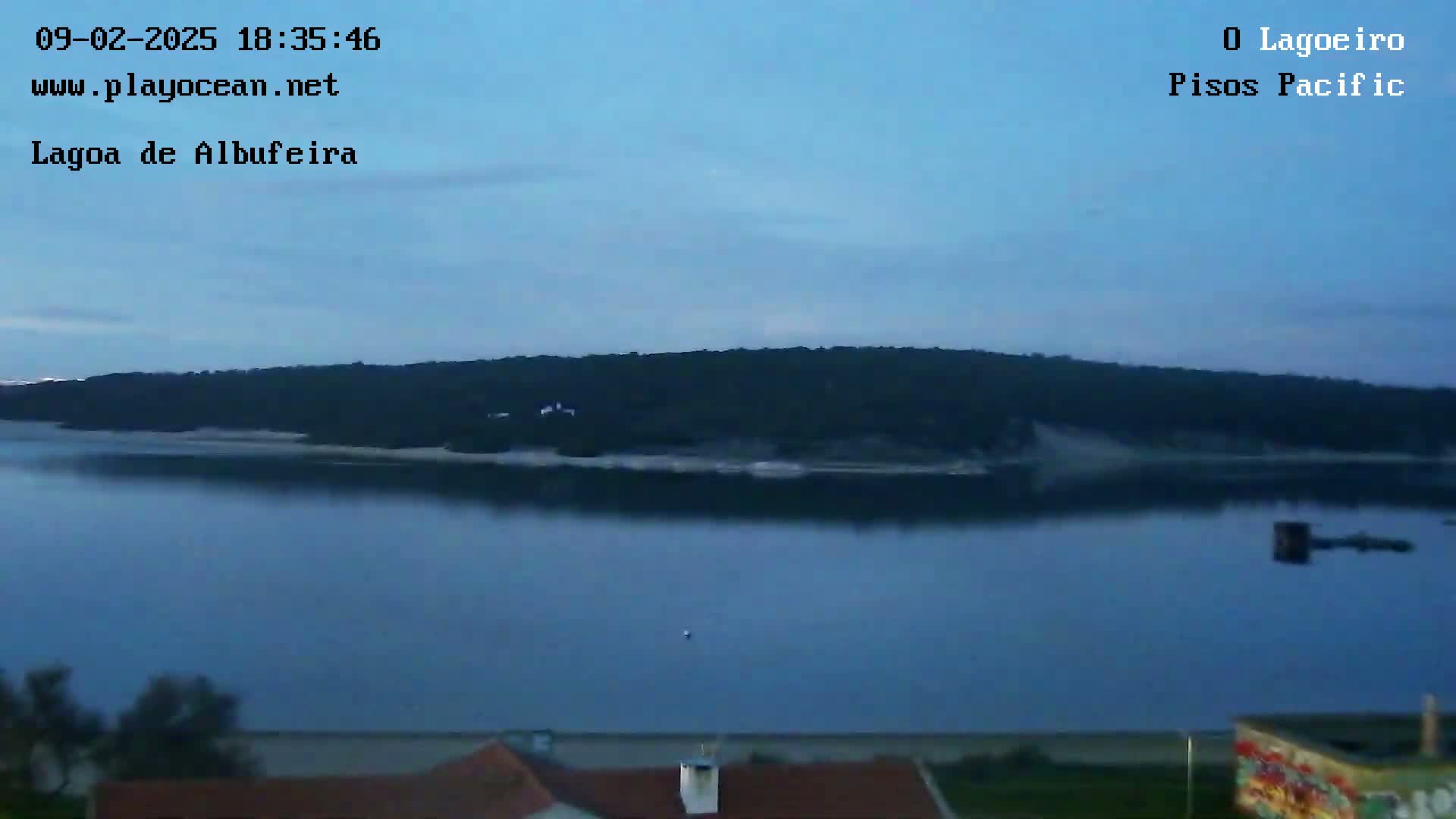 A calm, dark-blue body of water reflects a tree-covered landmass under a twilight sky.