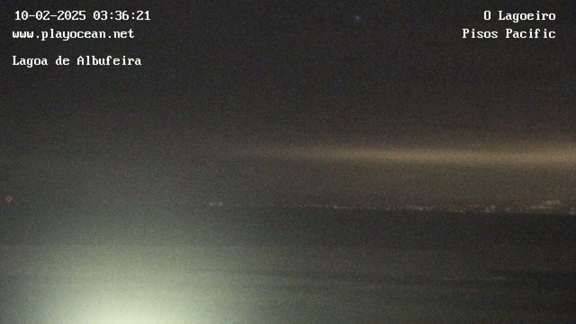 A nighttime long shot shows a dark horizon line with a faint glow of lights in the distance under a mostly clear, dark sky.