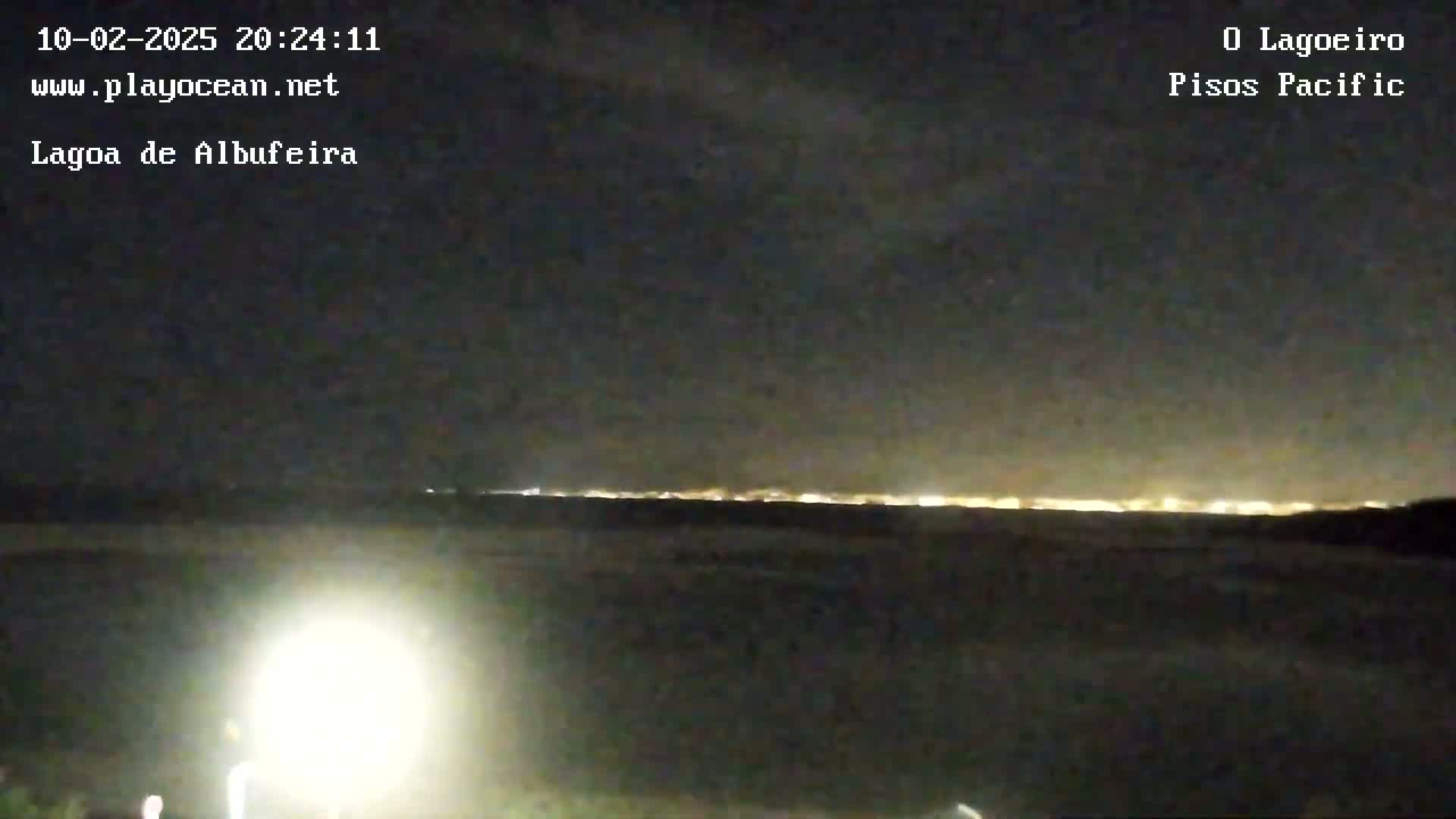A nighttime view shows a distant line of city lights on the horizon under a dark, clear sky, illuminated by a bright light source in the foreground.