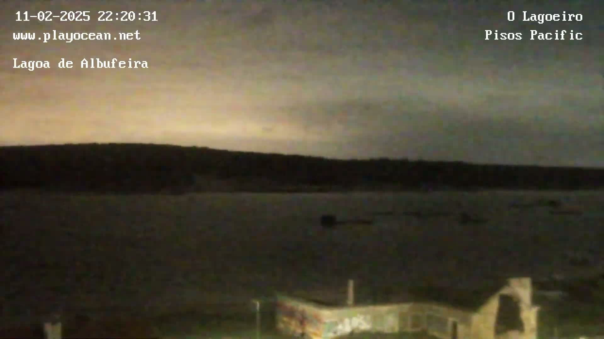 A dark, overcast night scene shows a body of water in front of a silhouetted shoreline.