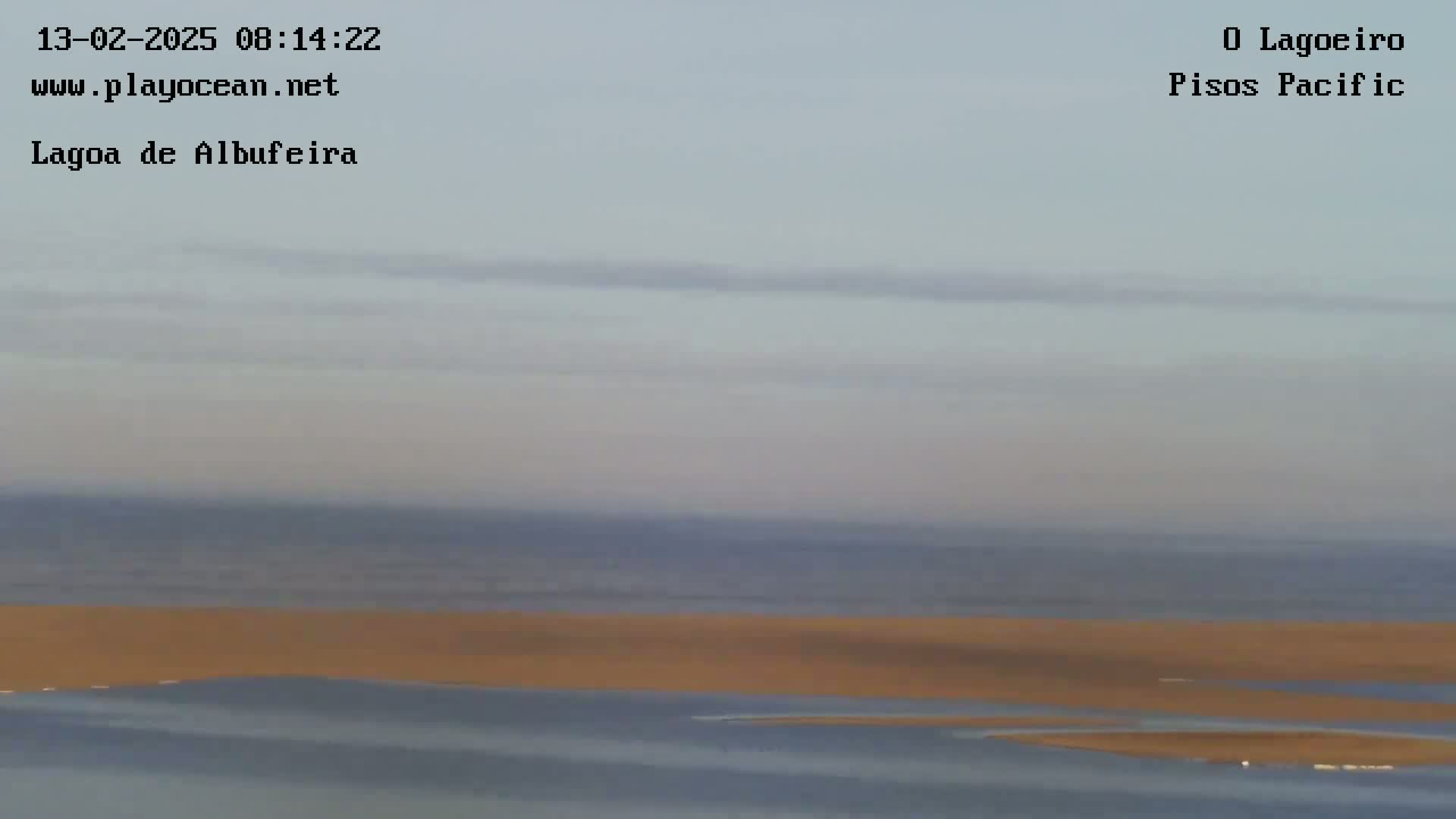 A calm, overcast day reveals a long stretch of sandy shoreline separating a body of water from the ocean.