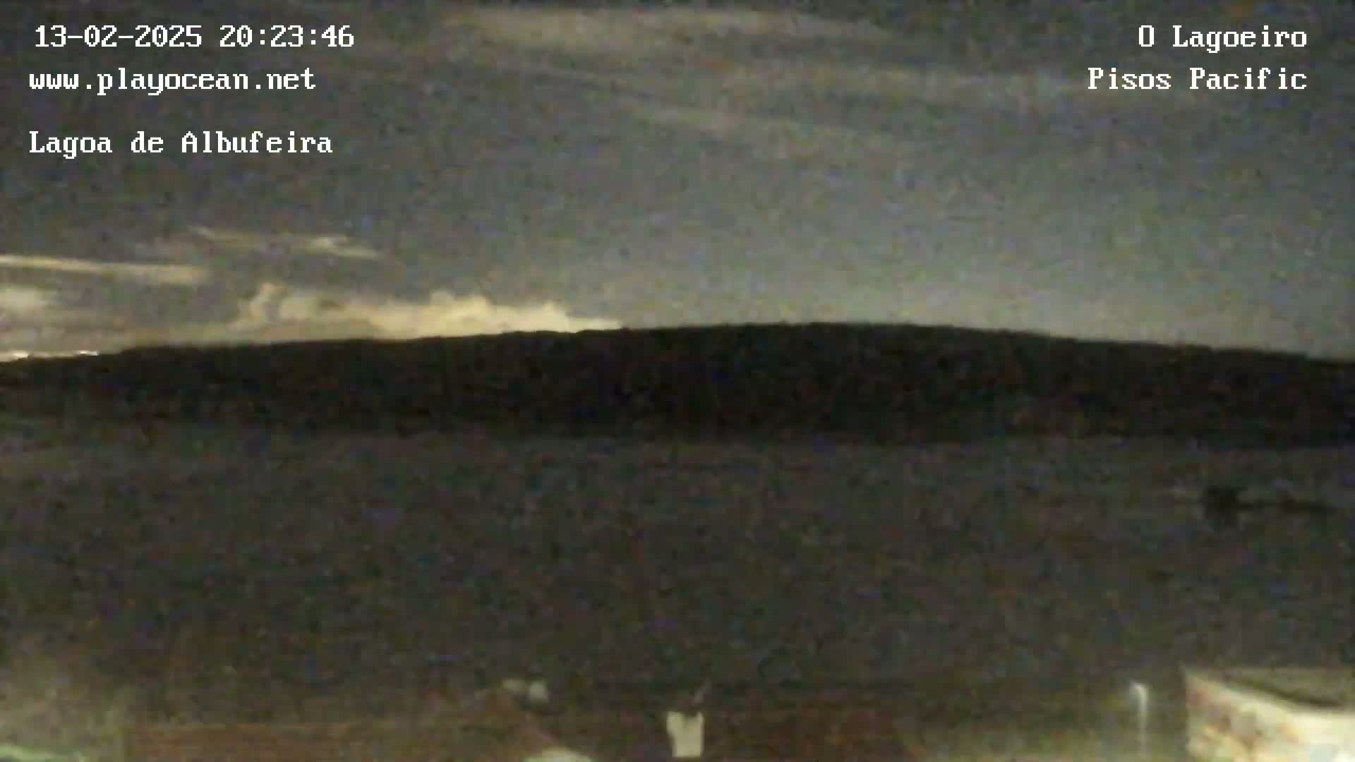 A dark, nighttime landscape shows a silhouetted line of land against a mostly cloudy sky with some faint light near the horizon.