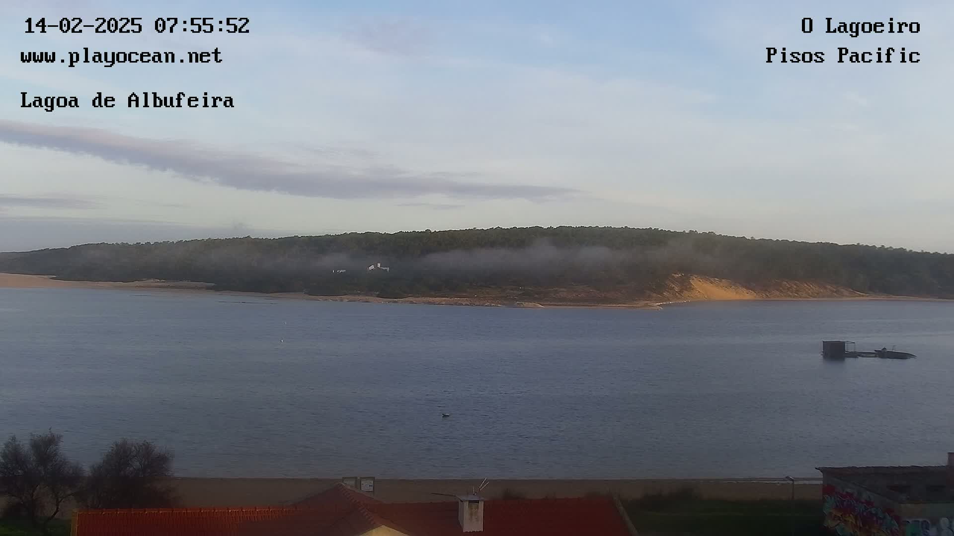 A calm body of water stretches out to a distant shoreline shrouded in morning mist, under a pale sky.