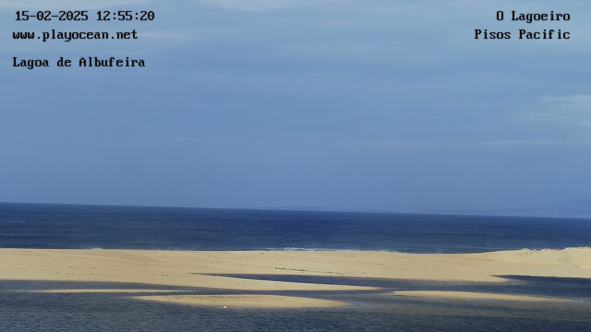 A sandy shoreline with calm water and a calm blue ocean under a clear sky.
