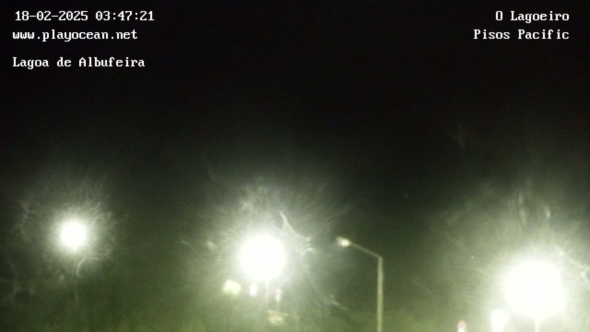 At night, under a hazy sky, several bright lights illuminate a dark roadway.