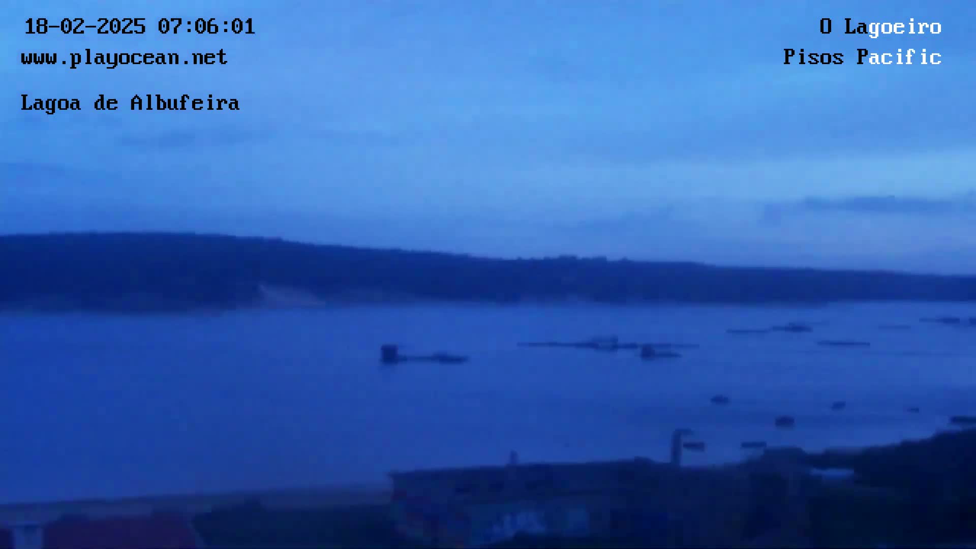 A calm, dark blue body of water stretches out before a dark shoreline under a twilight sky.