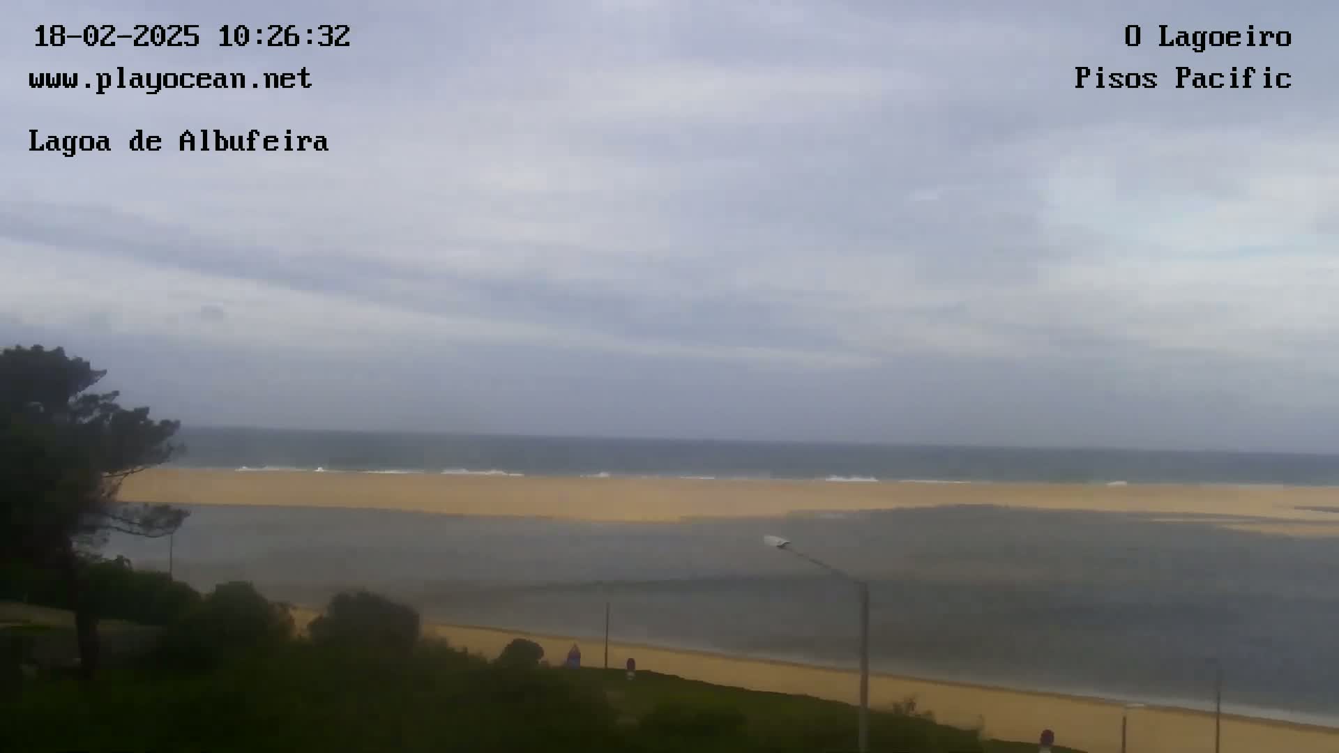 A view of a calm ocean meeting a sandy beach under an overcast sky.