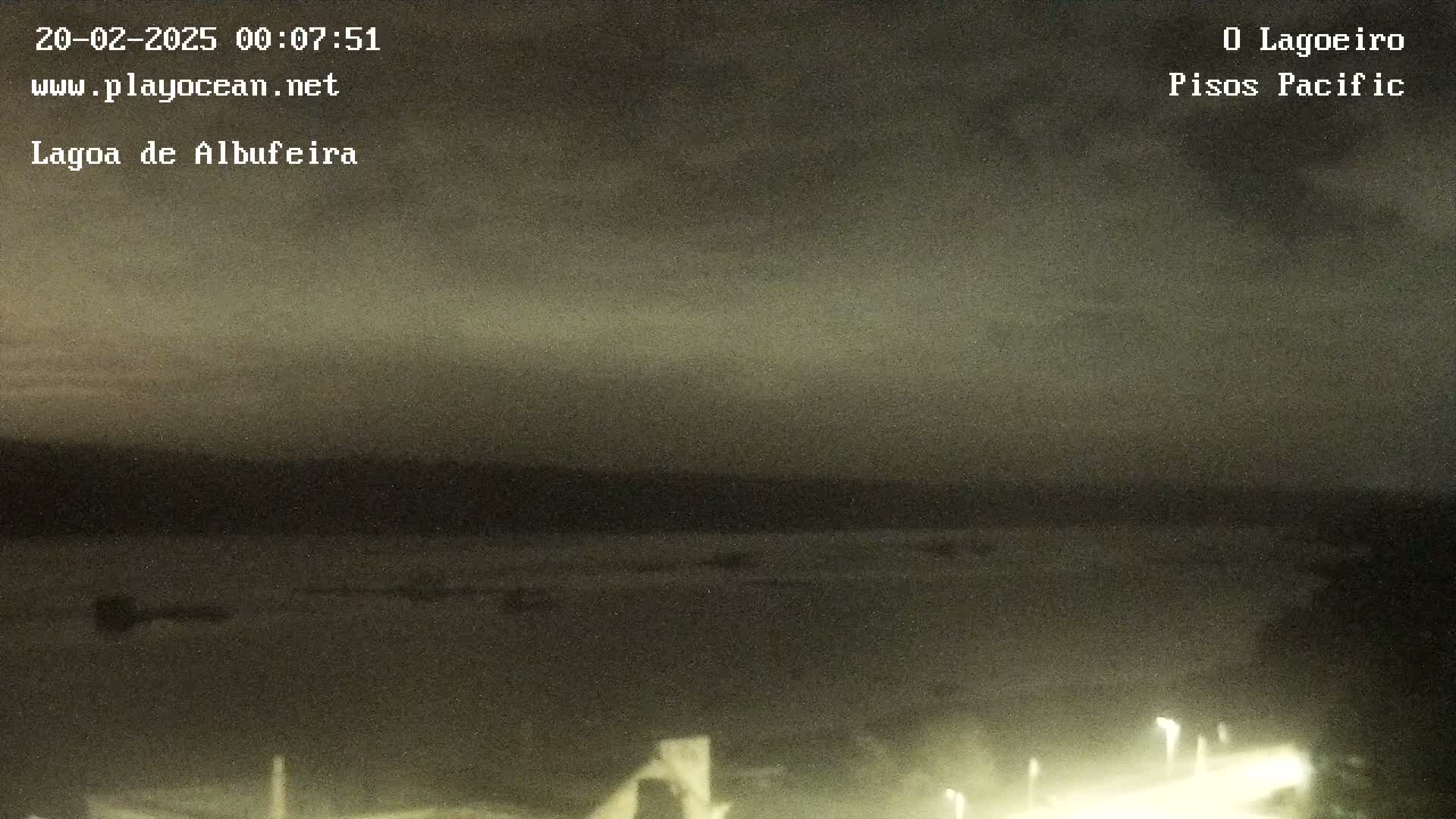 A dark, nighttime view of a calm body of water under a cloudy sky.