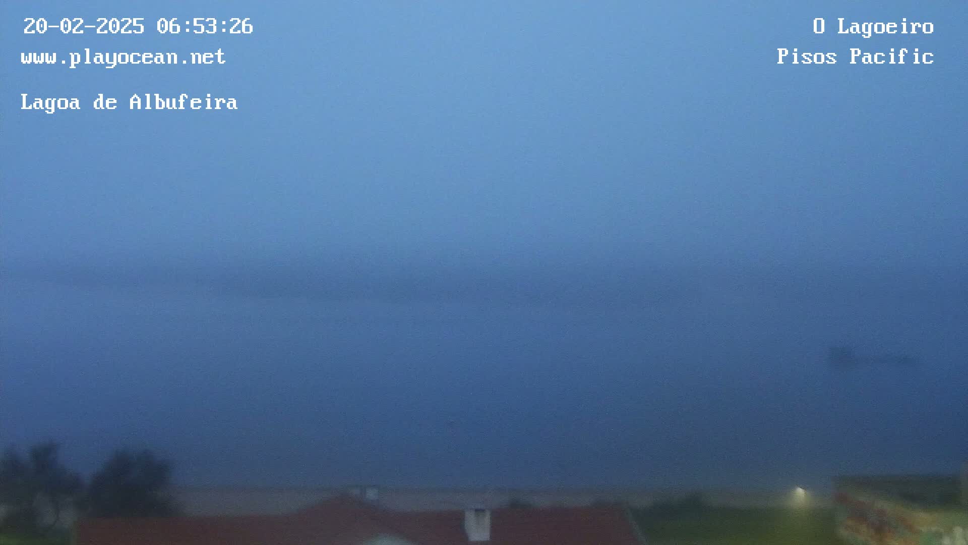 A foggy, dark blue body of water is visible from a low vantage point, with the tops of buildings and some vegetation barely visible in the foreground.