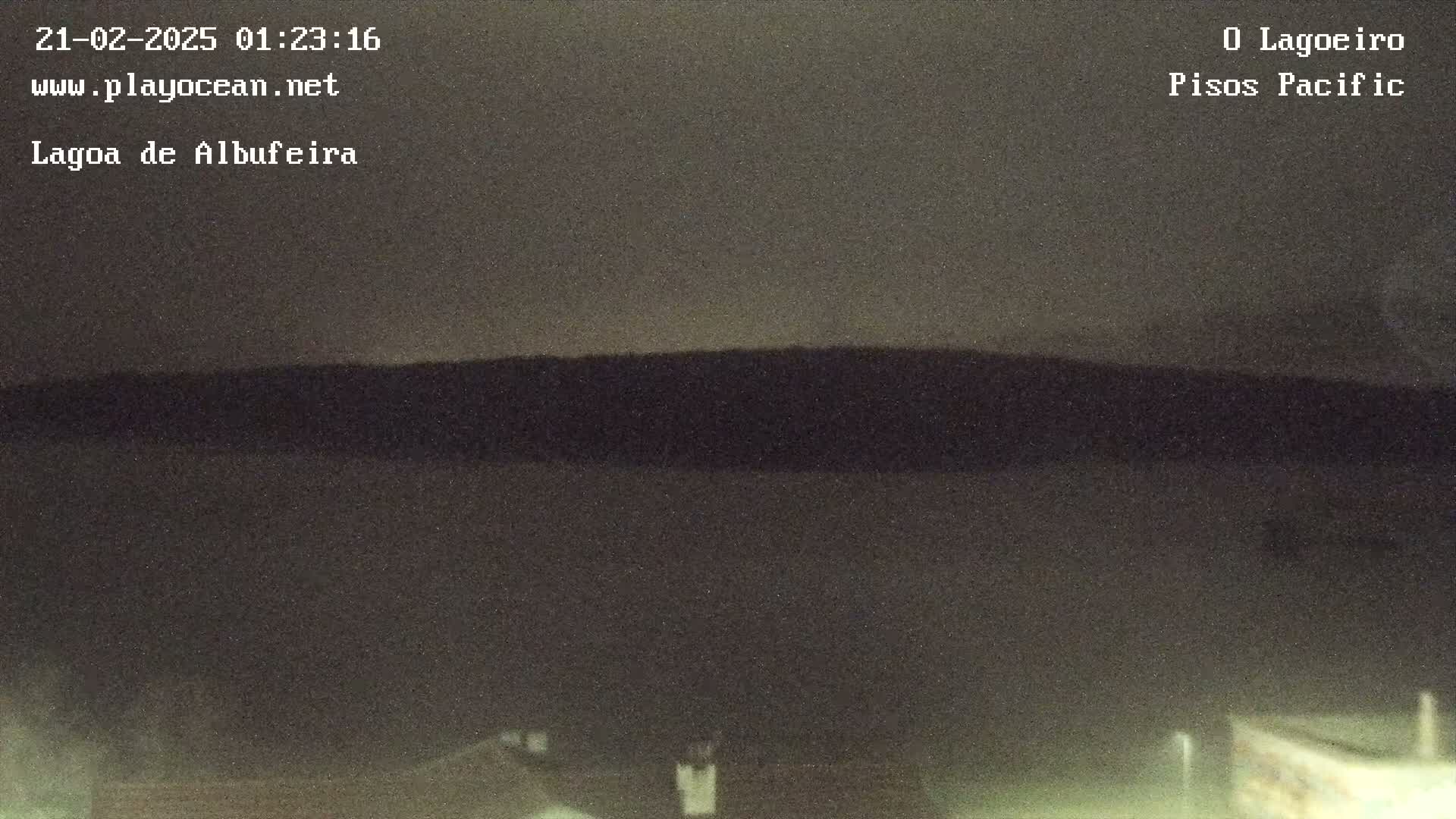 A dark, nighttime landscape shows a flat, dark body of water in the foreground and a dark hill in the background under a mostly clear, dark sky.