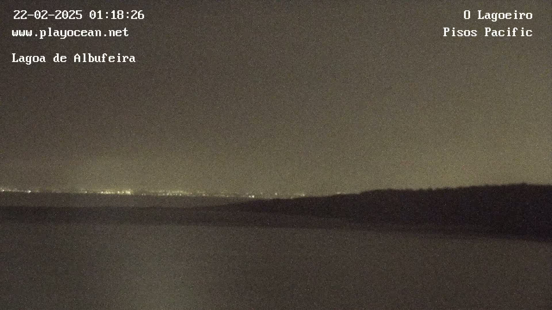 A nighttime, long-range view shows a dark, flat landscape with a distant line of lights on the horizon.