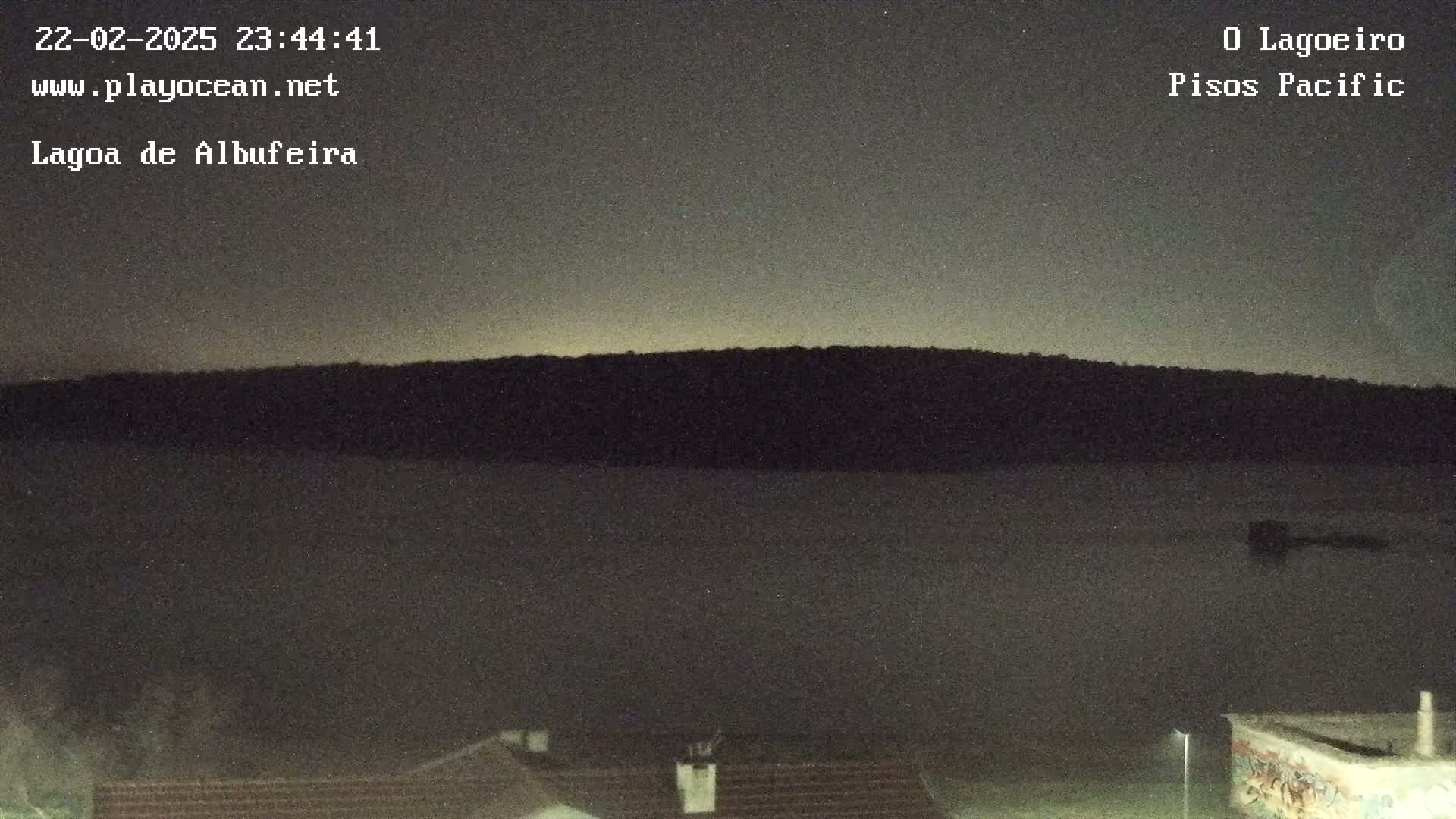 A dark, nighttime view shows a body of still water in front of a silhouetted hill under a mostly clear sky.
