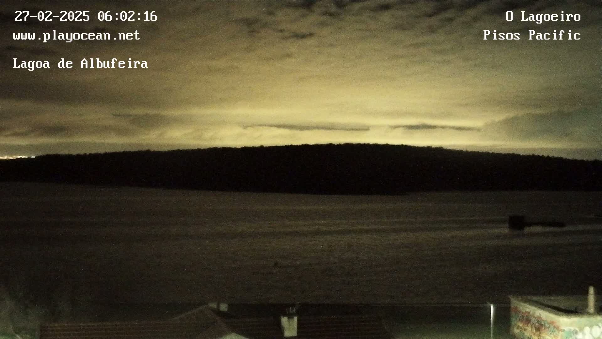 A dark, still body of water is visible beneath a cloudy, yellowish night sky, with a dark shoreline in the distance.