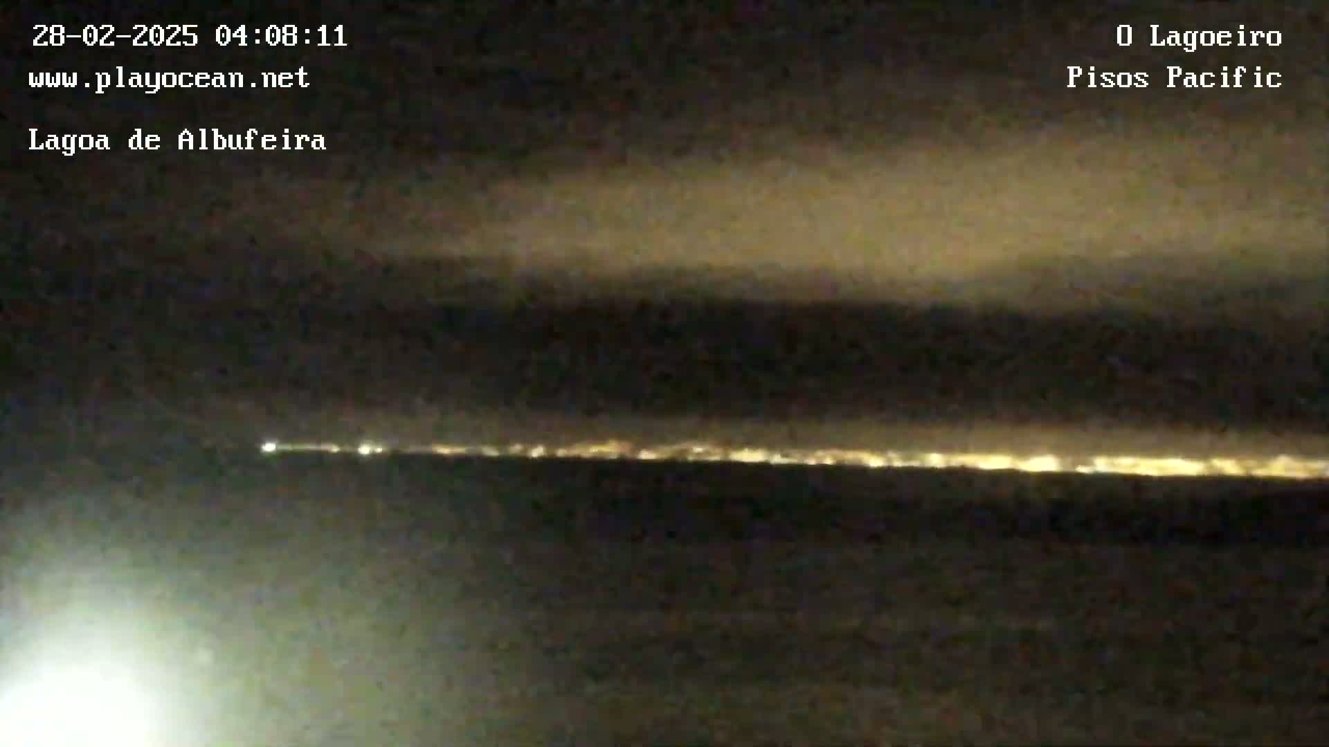 A nighttime long shot shows a distant line of lights on the horizon under a dark, cloudy sky.