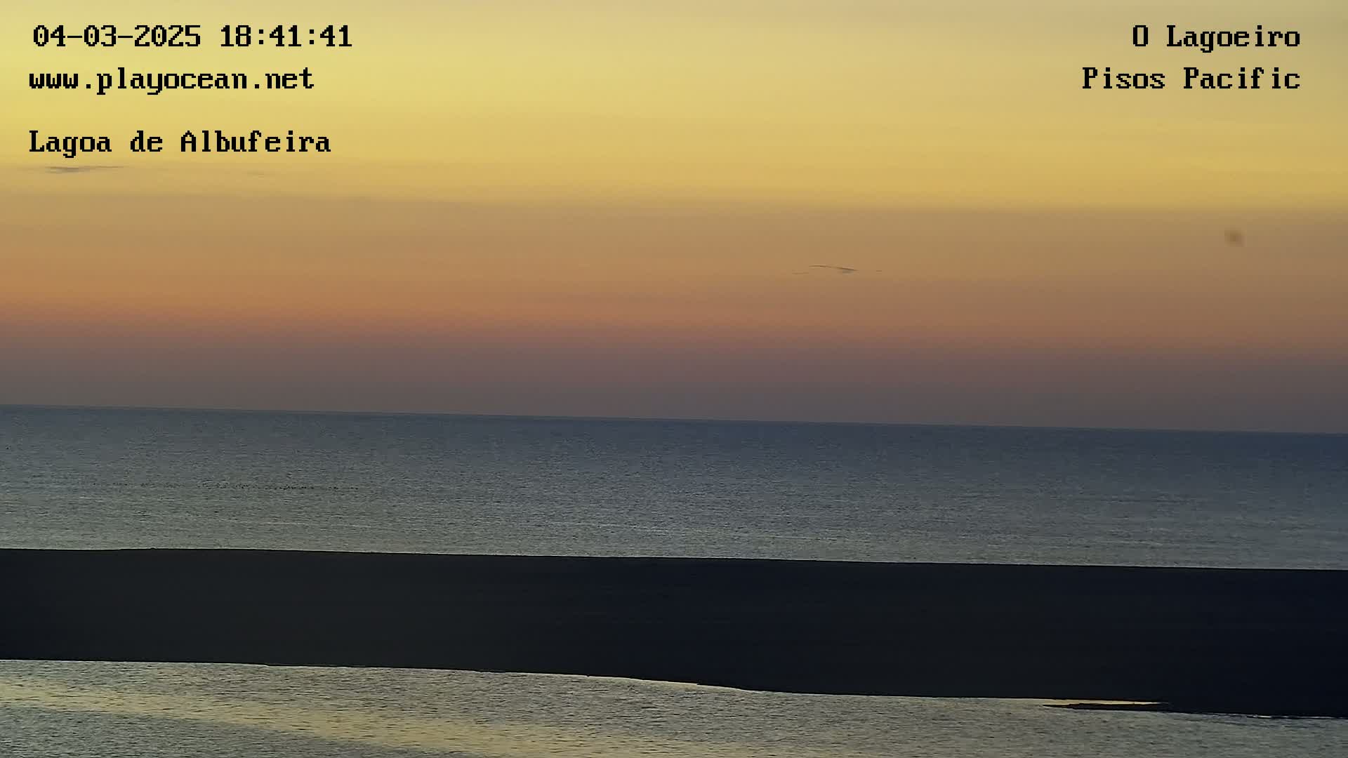 A calm ocean meets a dark shoreline under a sunset sky.