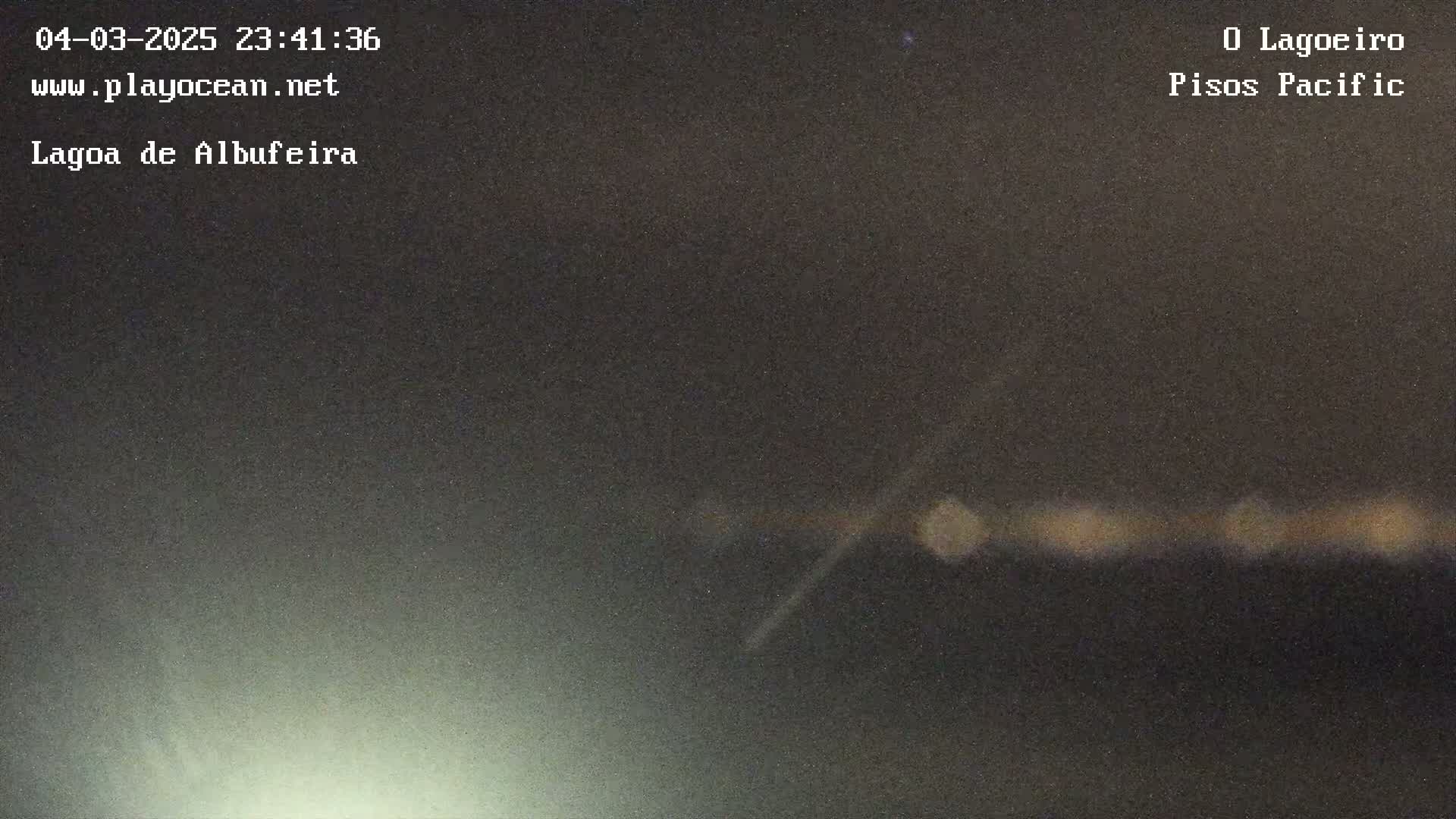 A blurry, nighttime image shows a dark, hazy sky over a faint line of lights on the horizon.