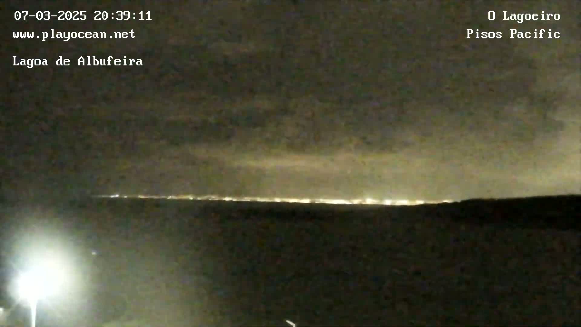 A nighttime view shows a distant line of city lights on the horizon under a cloudy sky.