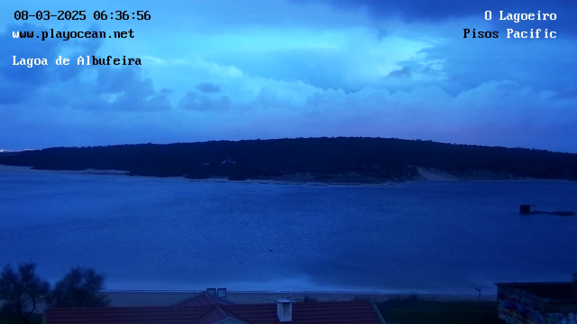 A dark blue body of water stretches to a dark shoreline under a twilight sky filled with clouds.