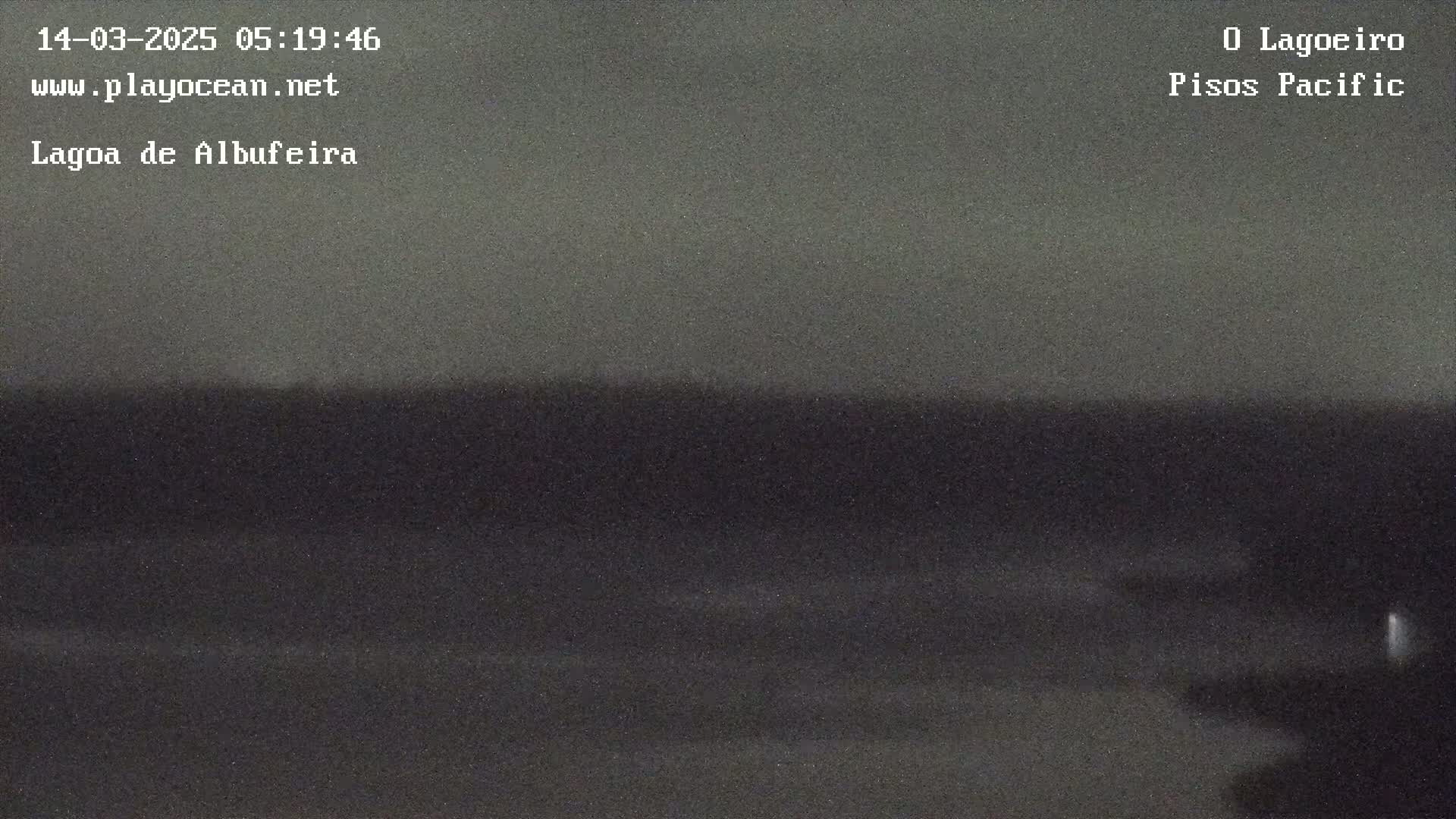 A dark, nighttime view of a body of water shows a relatively calm surface with faint waves near the shore.